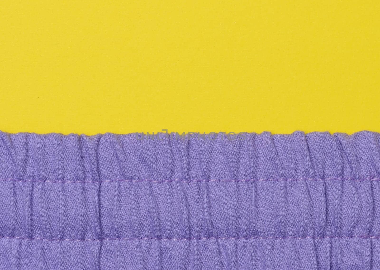 Fragment of purple fabric with an elastic band on a yellow background