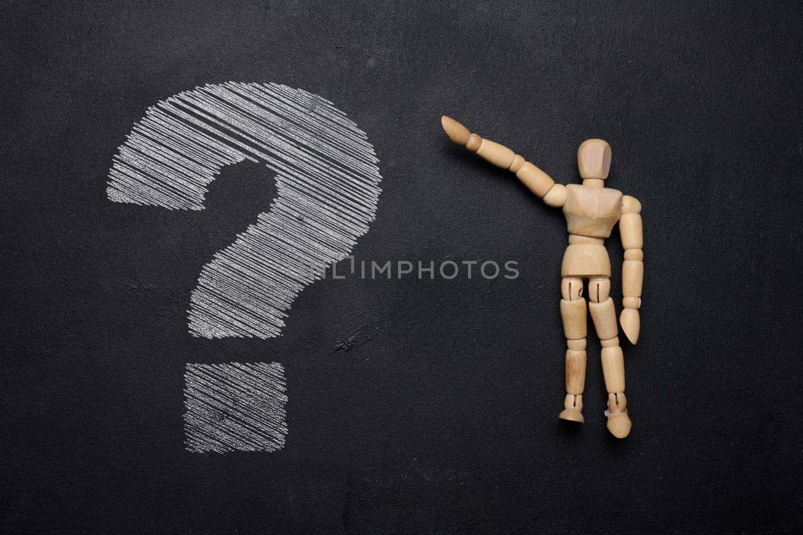 A wooden mannequin and a white chalk-drawn question mark on a black board, depicting the concept of uncertainty and curiosity