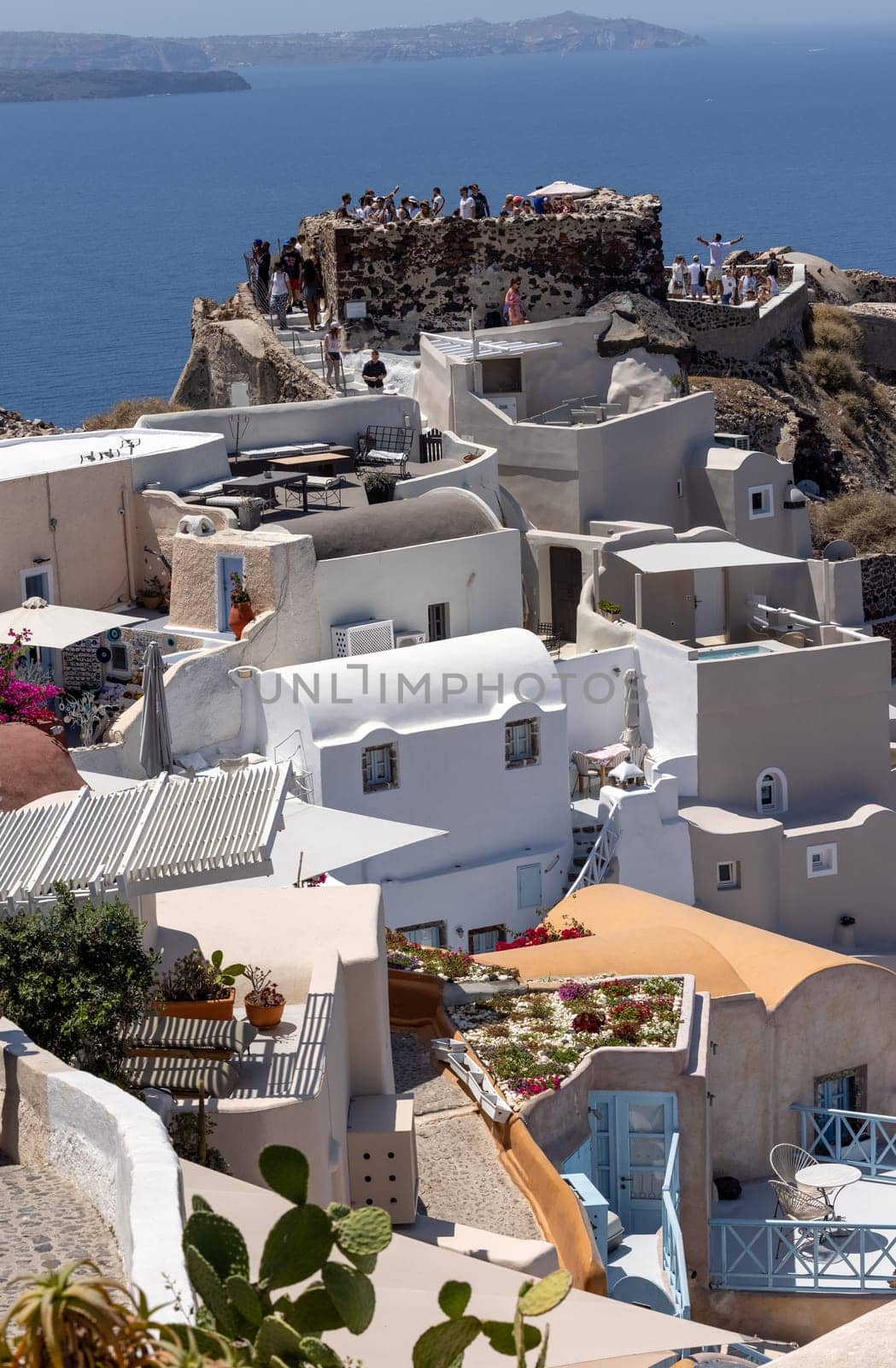 Oia, Santorini, Greece - July 3, 2021: Whitewashed buildings and the ruins of Castle of Agios Nikolaos on the edge of the caldera cliff, Oia village, Santorini, Greece