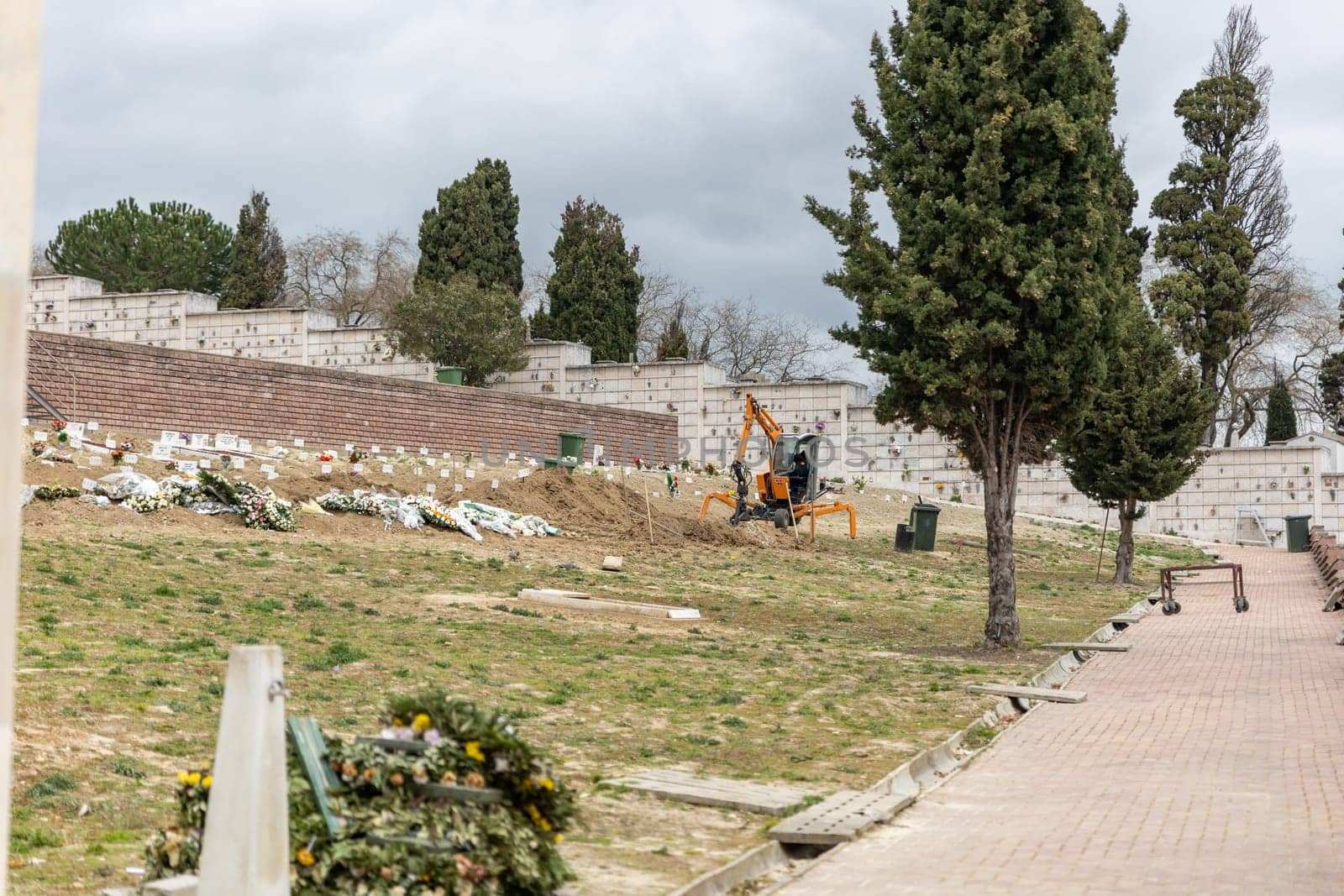 February 22, 2023 Lisbon, Portugal: Alto de Sao Joao Cemetery - excavator digs up the earth for the grave. Mid shot