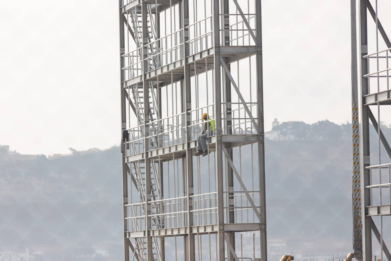 Construction site - a black worker sits at the height of the building frame. Mid shot
