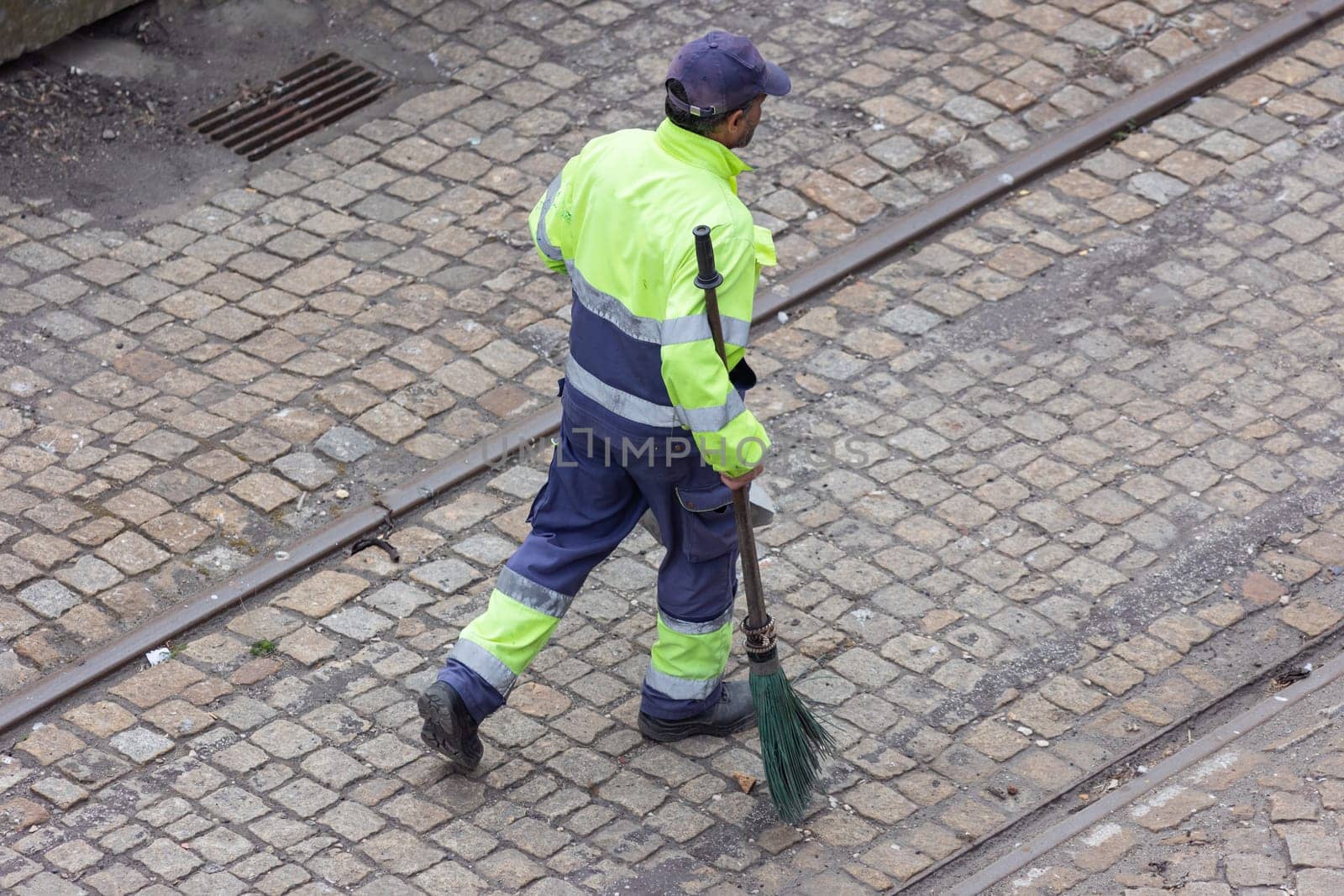 A worker reflective vest walks on the street with a broom. Mid shot
