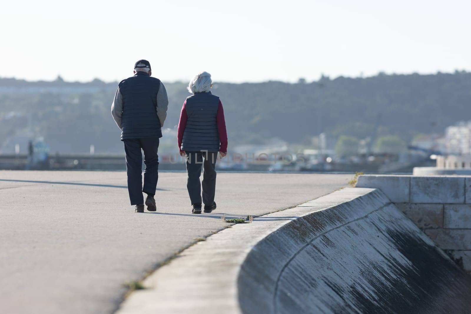 An elderly couple walks along the embankment near a concrete slope. Mid shot