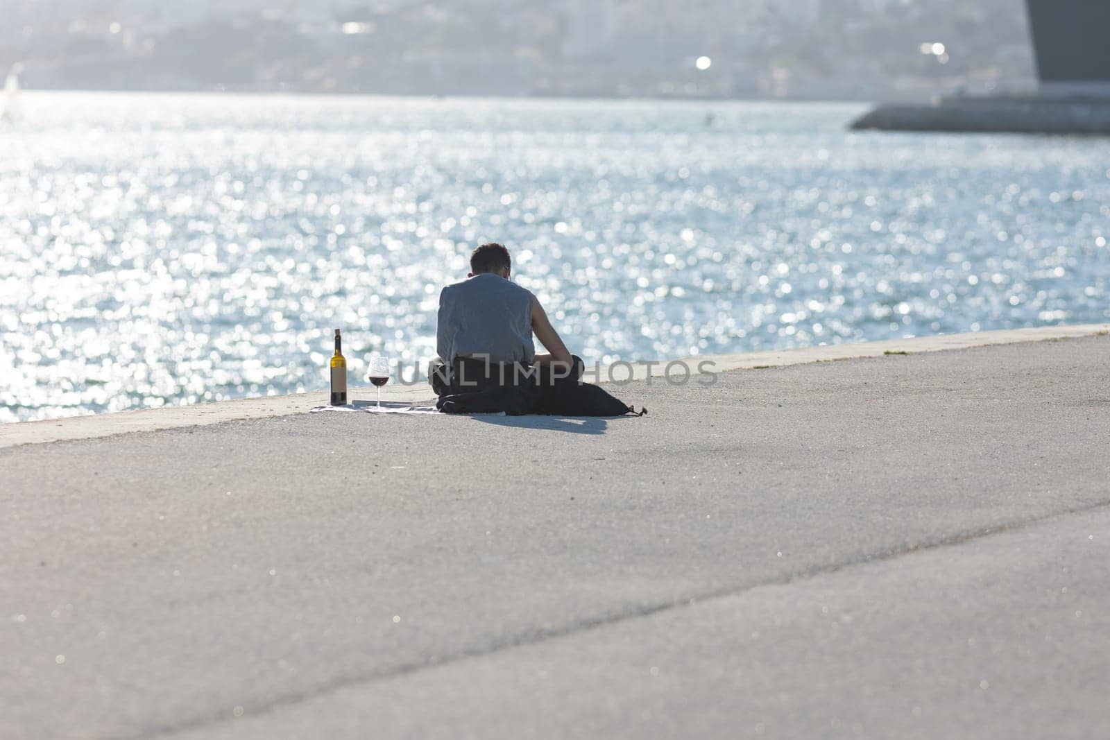 A lonely man drinking wine from a glass at the waterfront. Mid shot