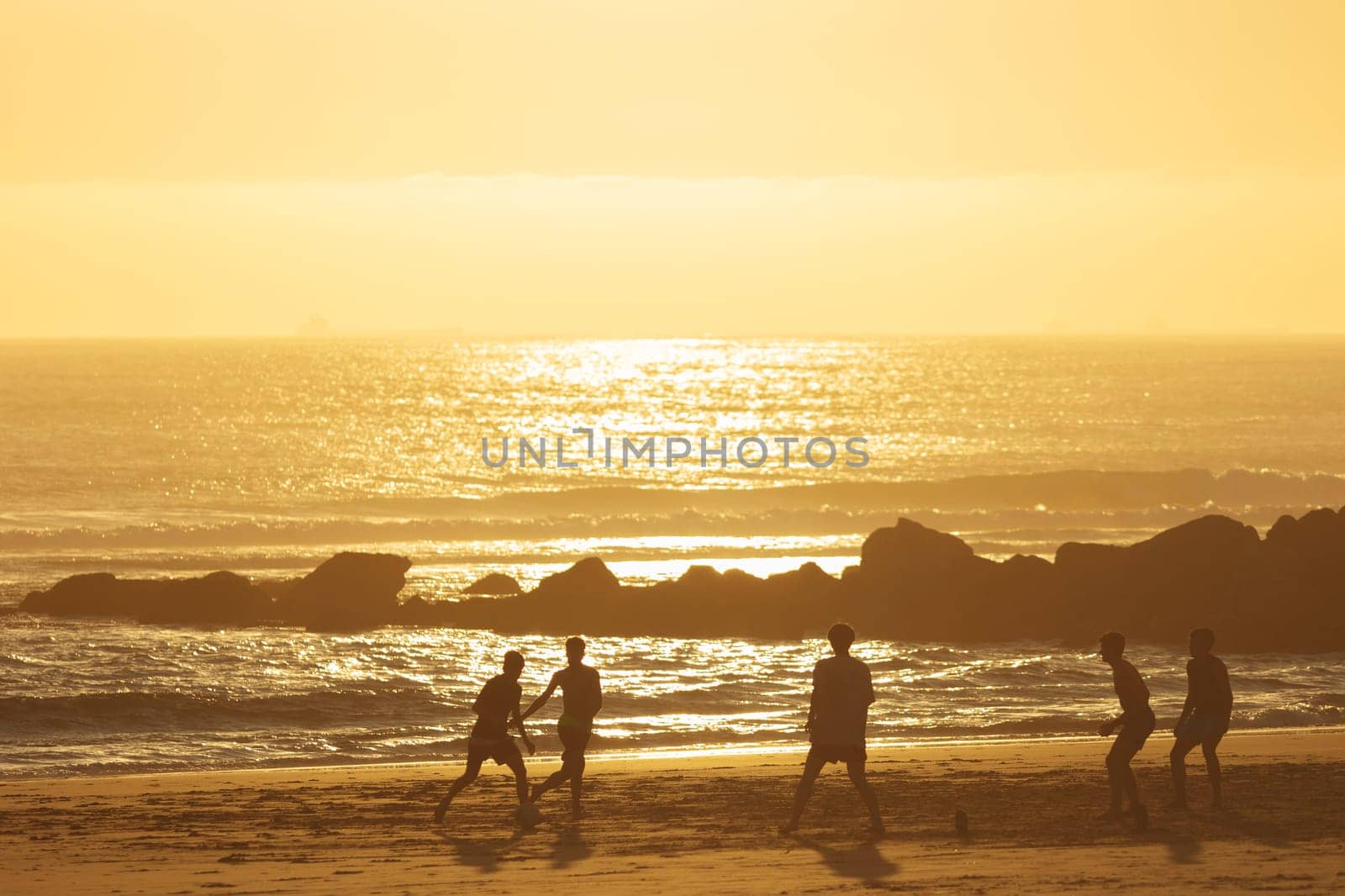 19 April 2023 Lisbon, Portugal: Costa da Caparica - young men playing ball on the beach at sunset. Mid shot