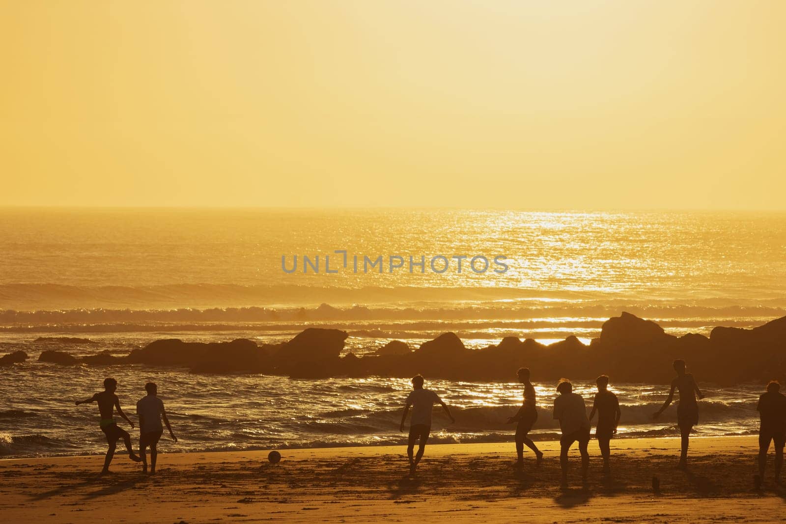 Teenage boys playing soccer on the beach at sunset. Mid shot