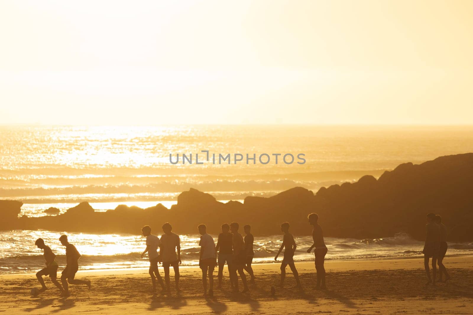 Young men playing a ball on the beach at sunset. Mid shot