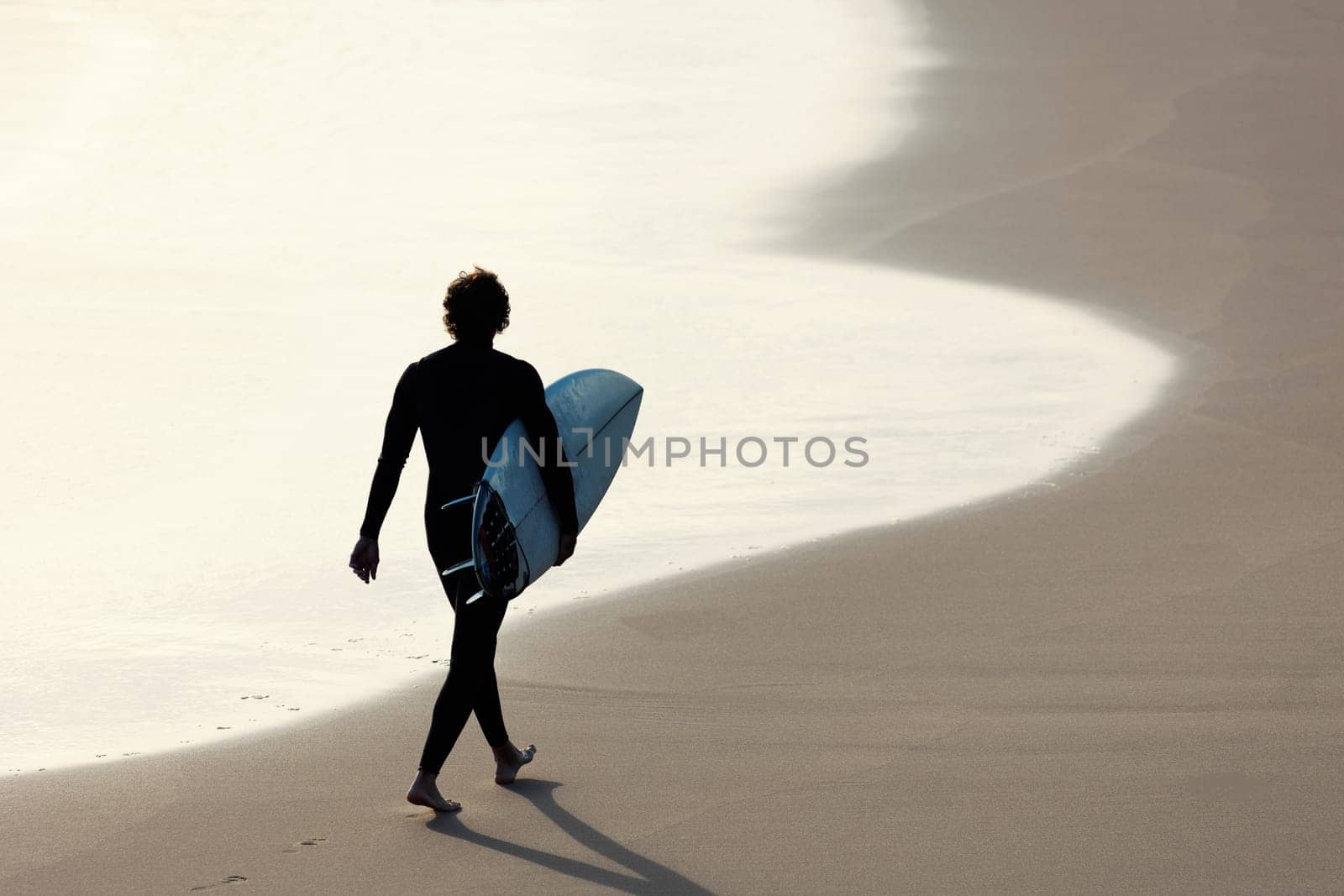 Black silhouette of a man with a surfboard walking on the beach. Mid shot
