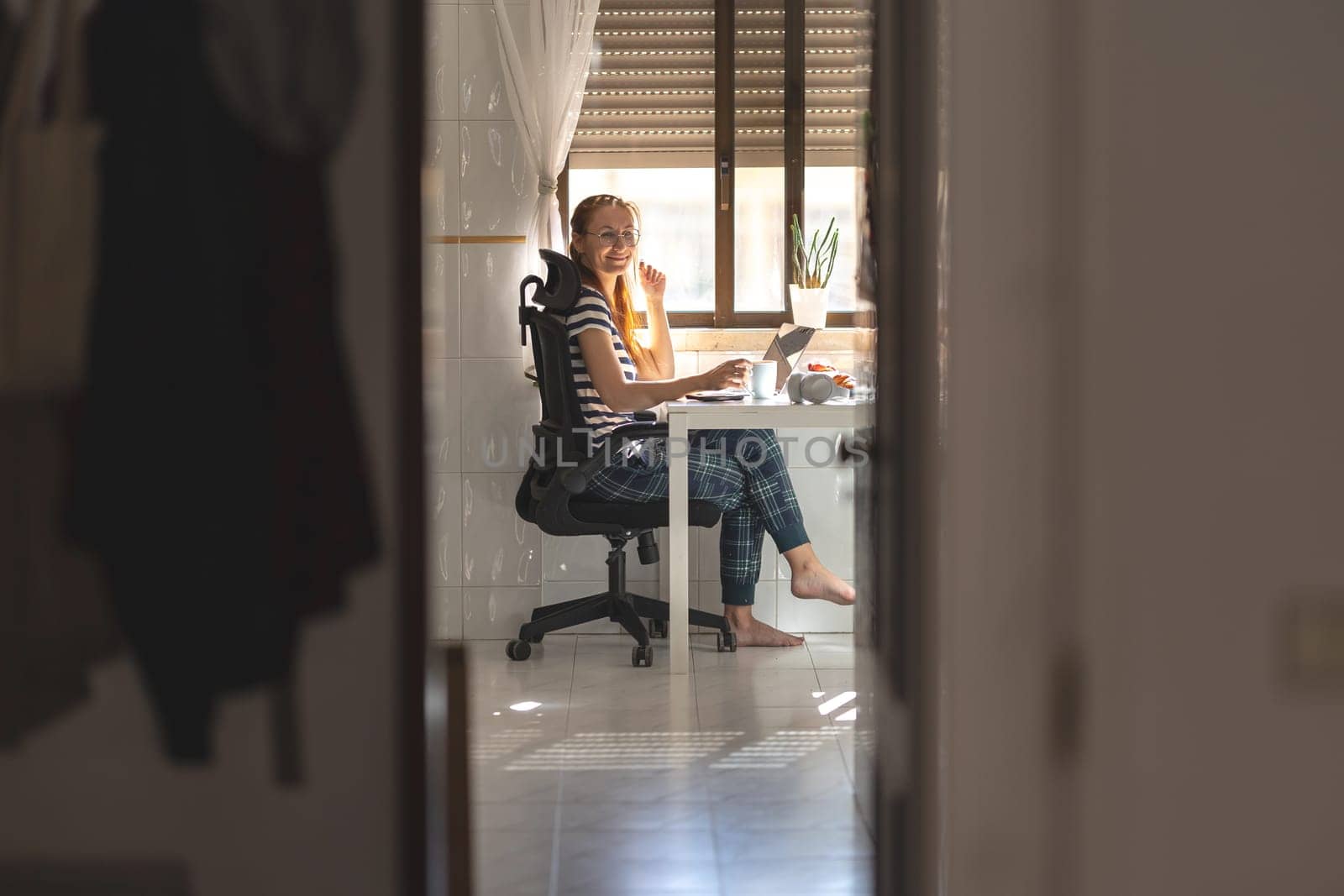 Smiling woman freelancer working at the kitchen table - looking in the camera. Mid shot