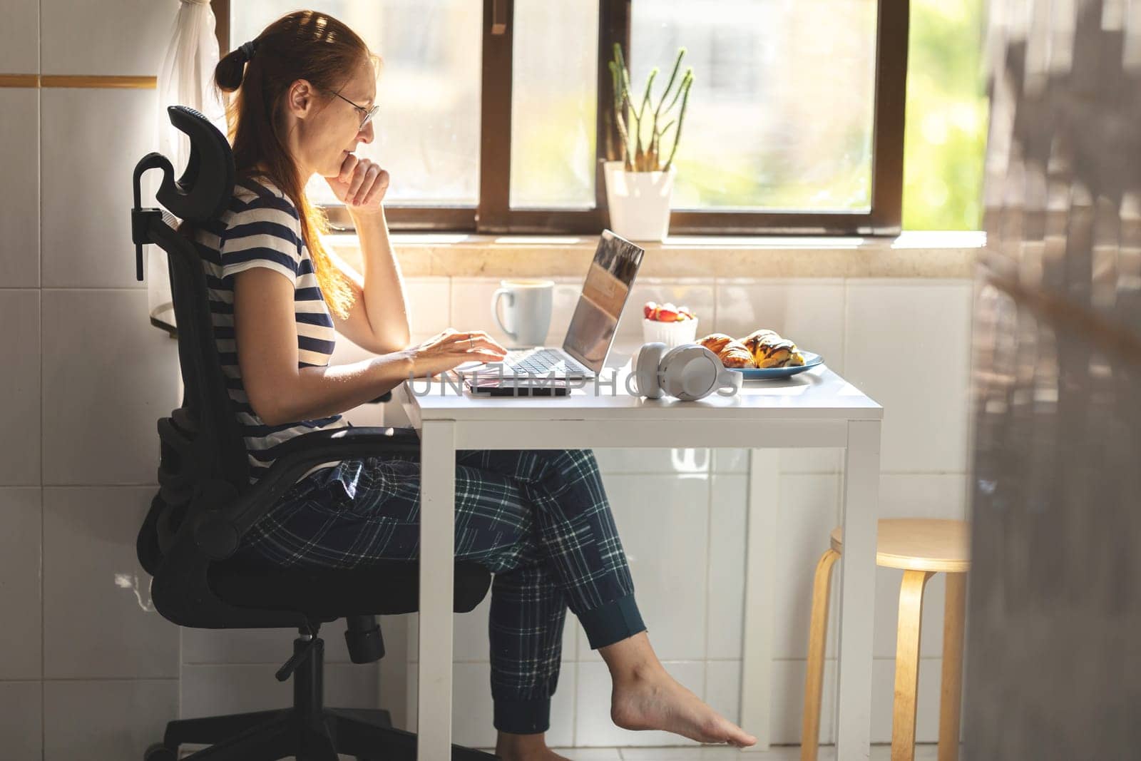 An adult woman freelancer working at the kitchen table. Mid shot