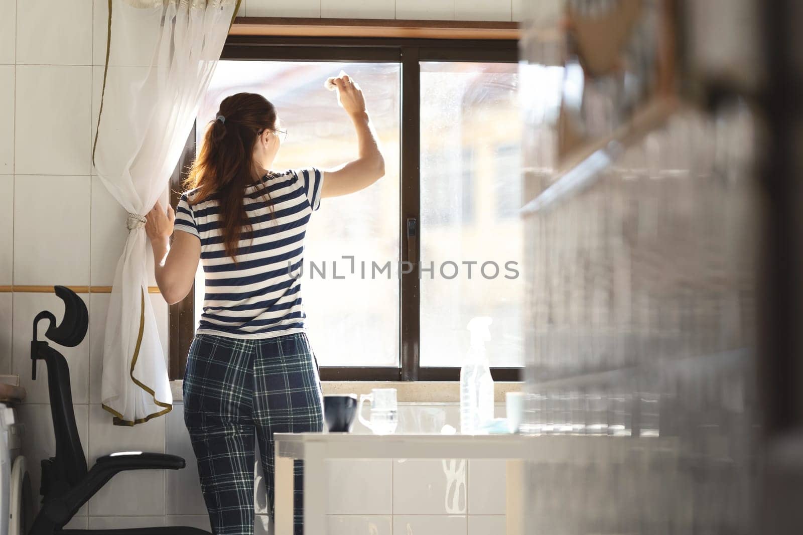 Adult woman housewife washing a window in the kitchen. Mid shot
