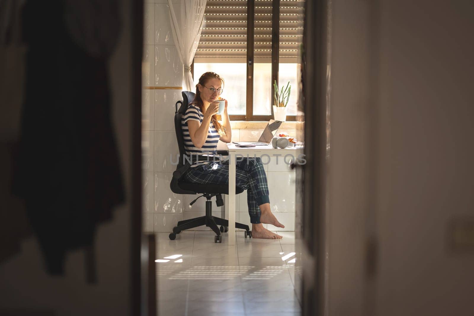 Adult woman with a cup of coffee at the kitchen table - looking in the camera. Mid shot