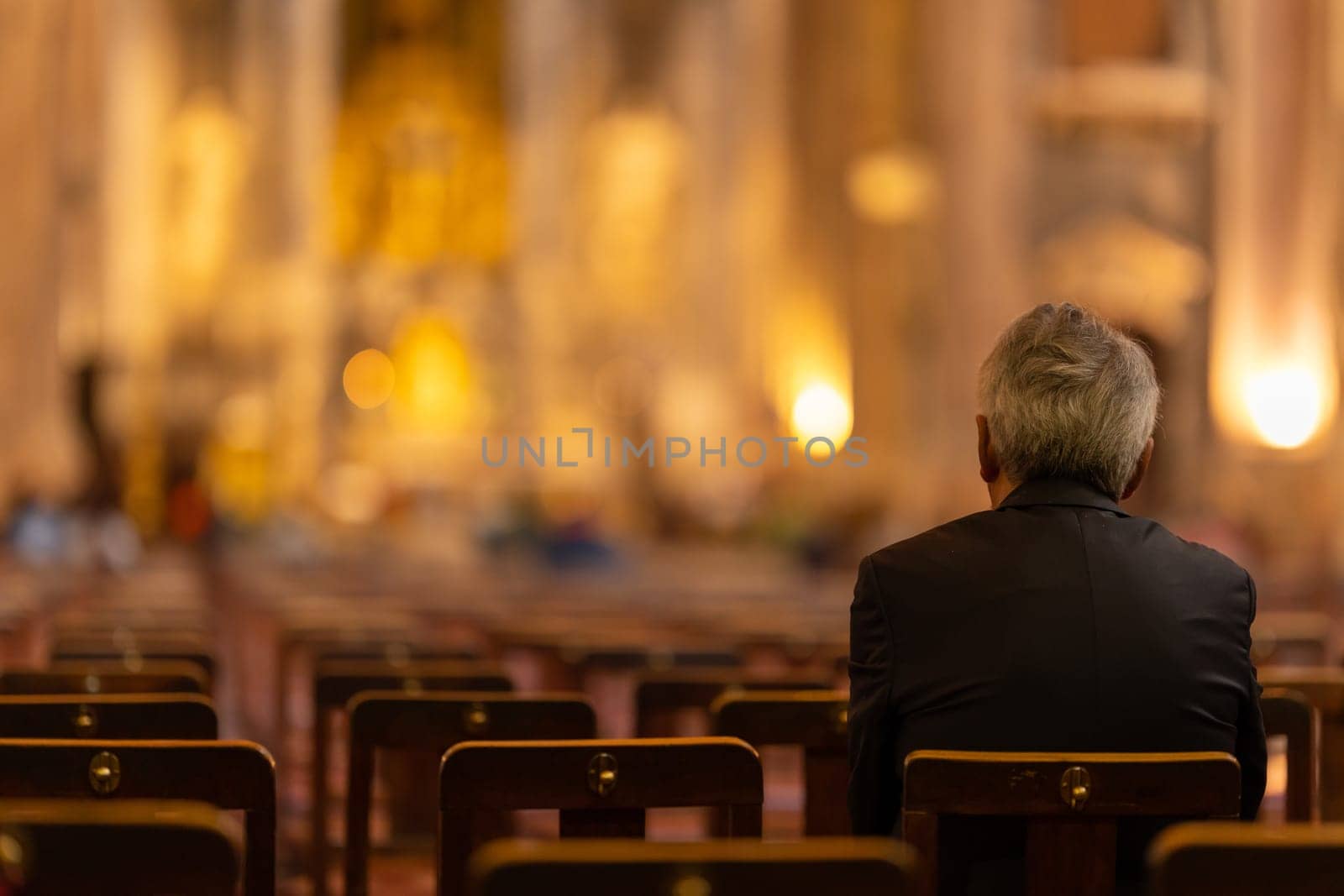 An elderly man sits on a chair in a church. Mid shot