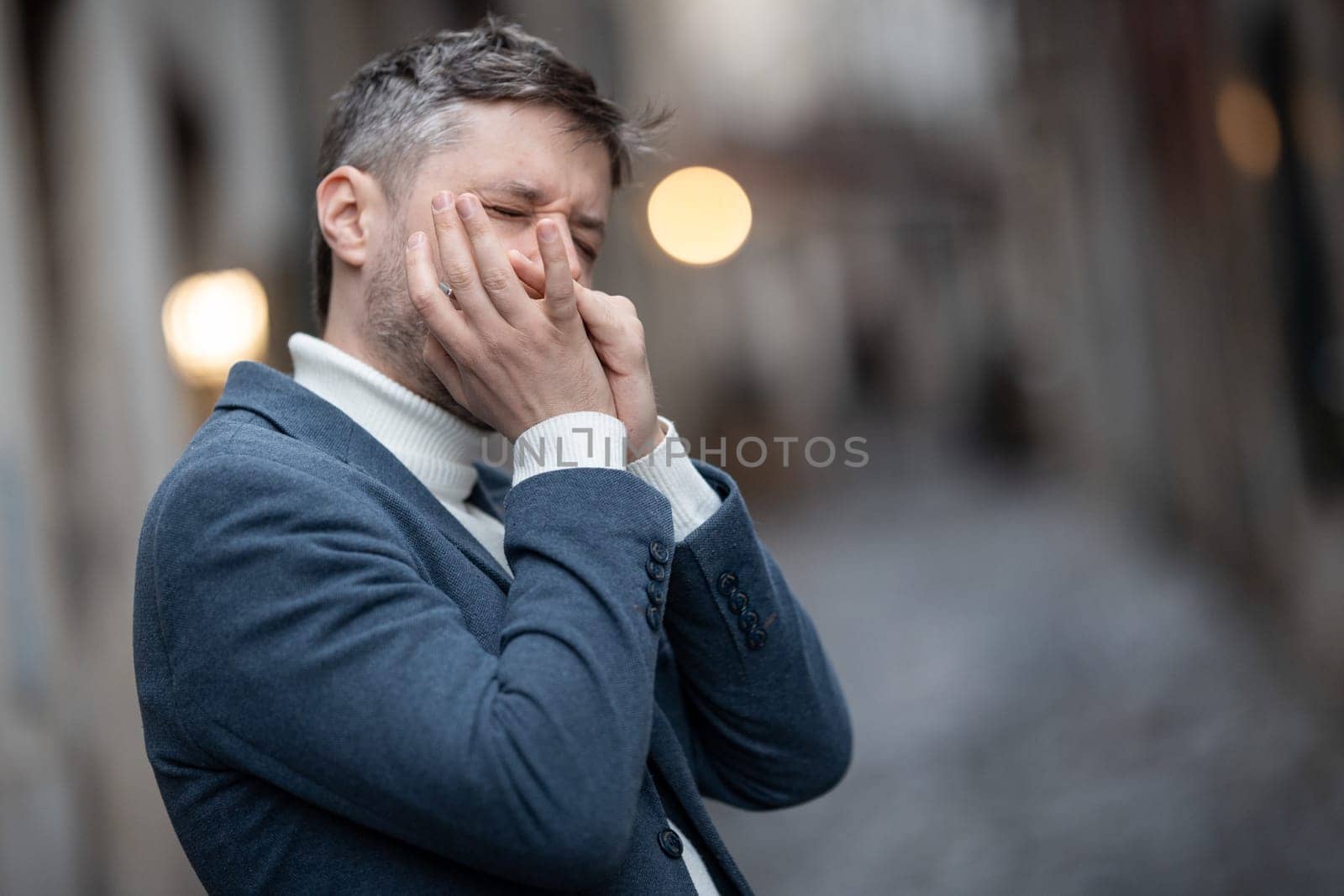 An adult man in blue jacket plays the harmonica on the street. Mid shot