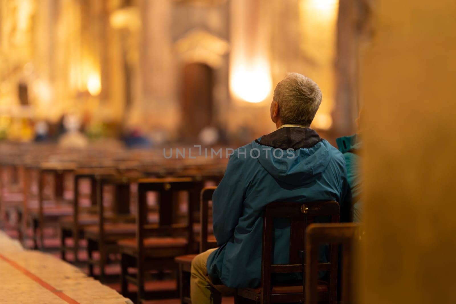 An elderly man sits at the entrance to the church and listens to a sermon. Mid shot