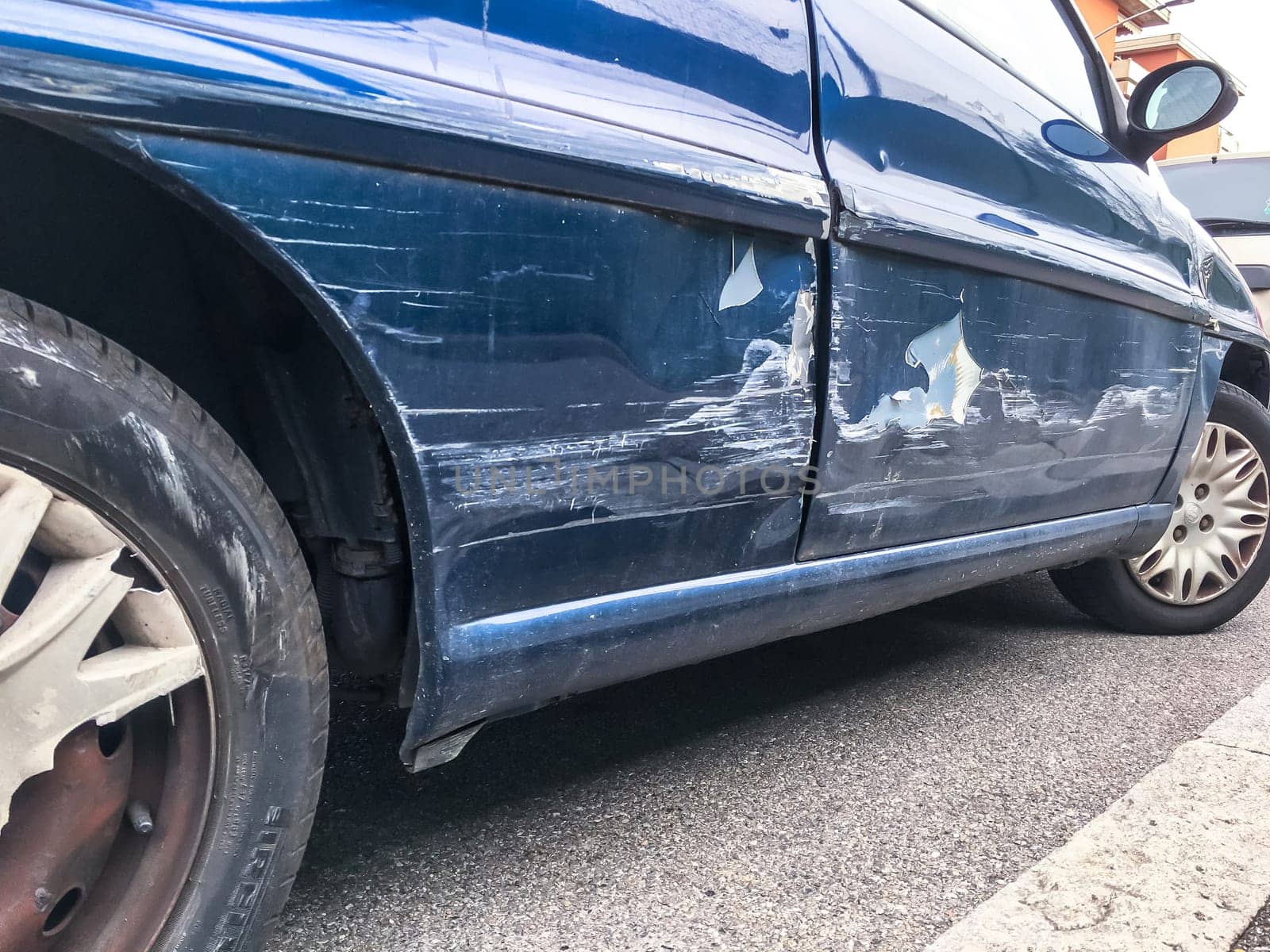 Blue car, dent in a door in the street after a broken accident.  Scratched car body. Dented.