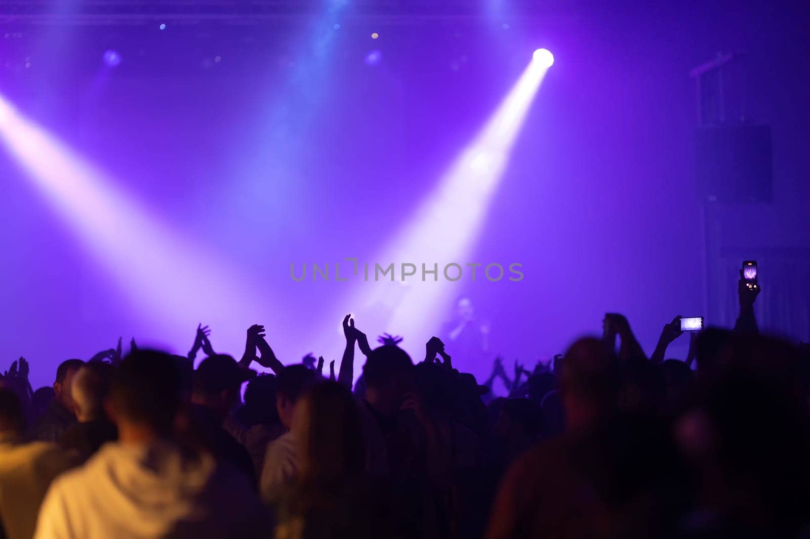 Bright lamps illuminate the stage at the concert - the silhouette of the crowd in the foreground. Mid shot