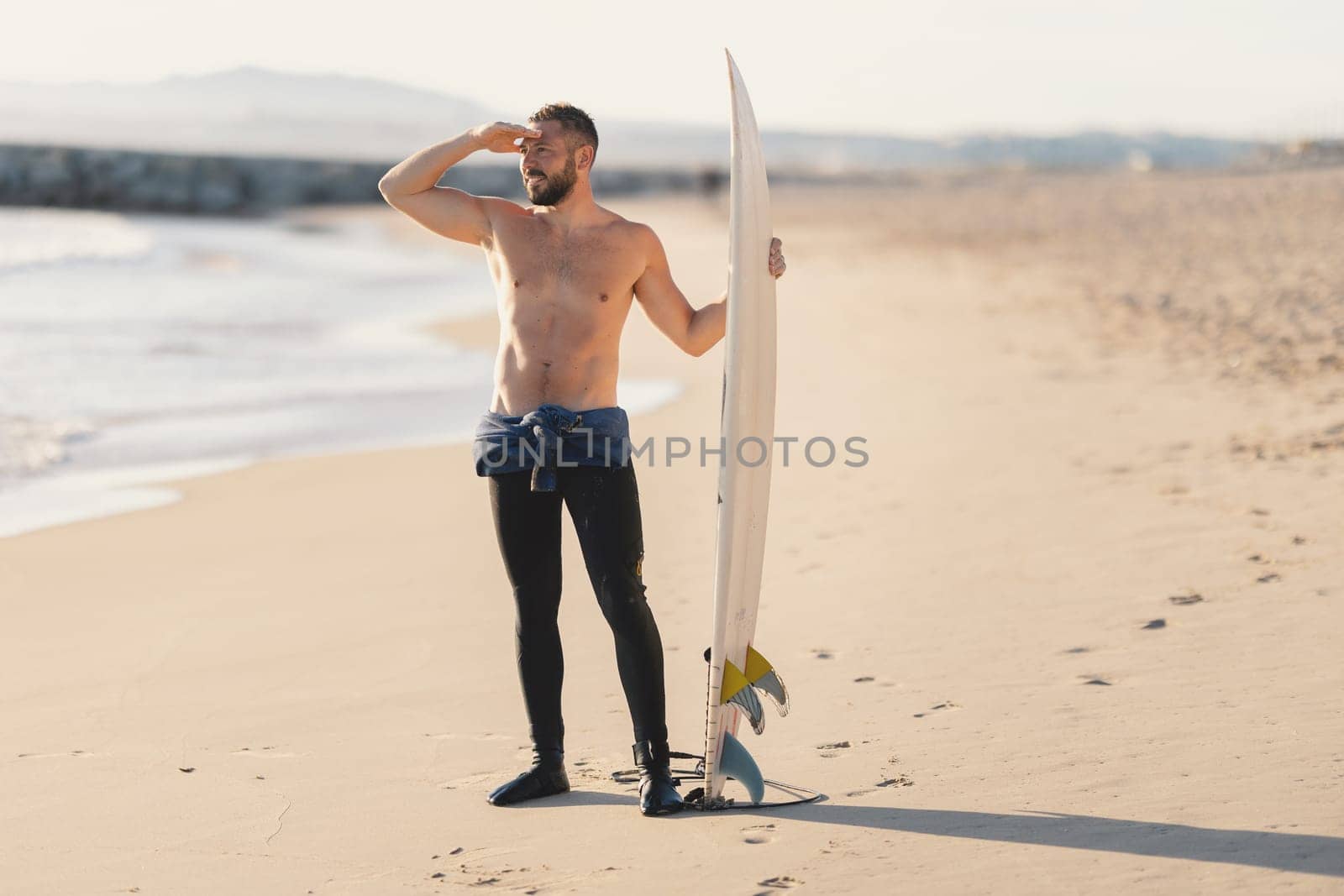 An athletic man surfer with naked torso looking in the distance. Mid shot