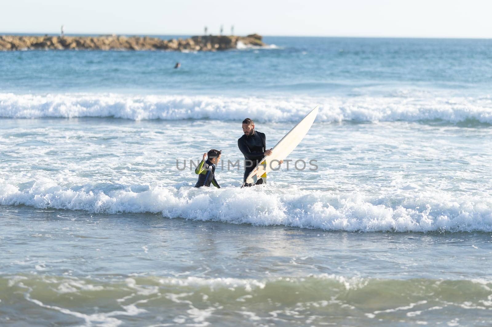 Father and son surfers in wetsuits in the sea. Mid shot