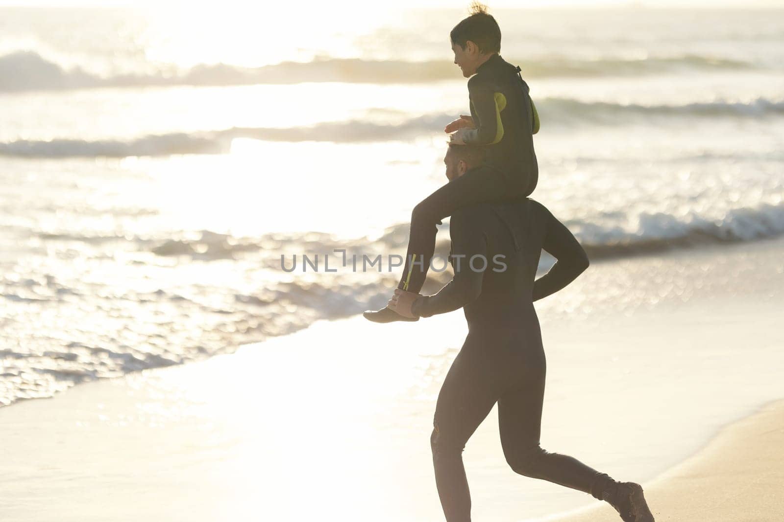 Little son on the shoulders of his father running to the sea at sunset. Mid shot