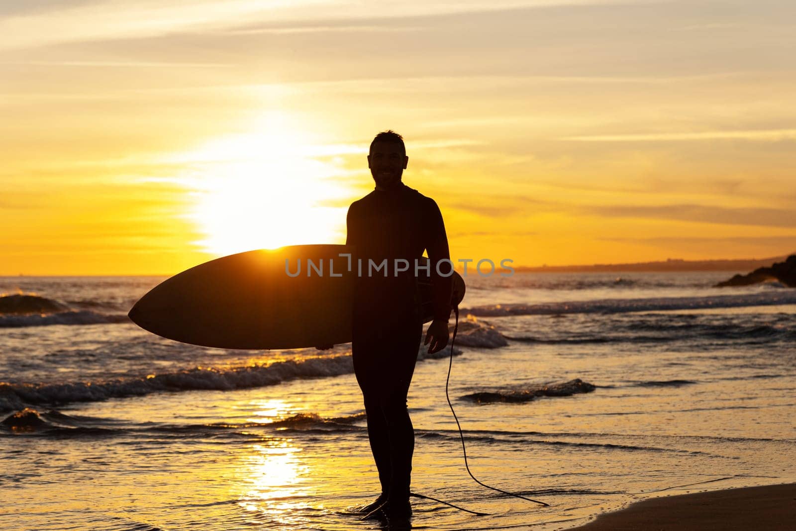 Silhouette of an athletic man surfer on the seashore. Mid shot