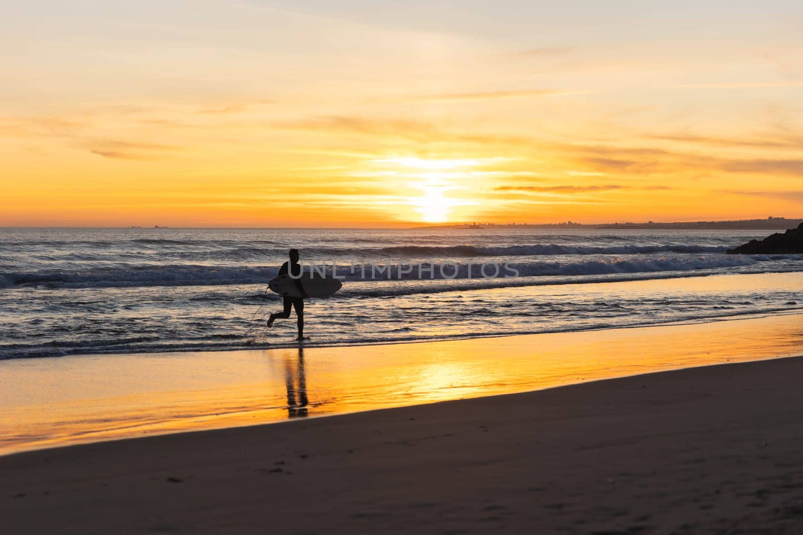 A man surfer running on the seashore at sunset. Mid shot