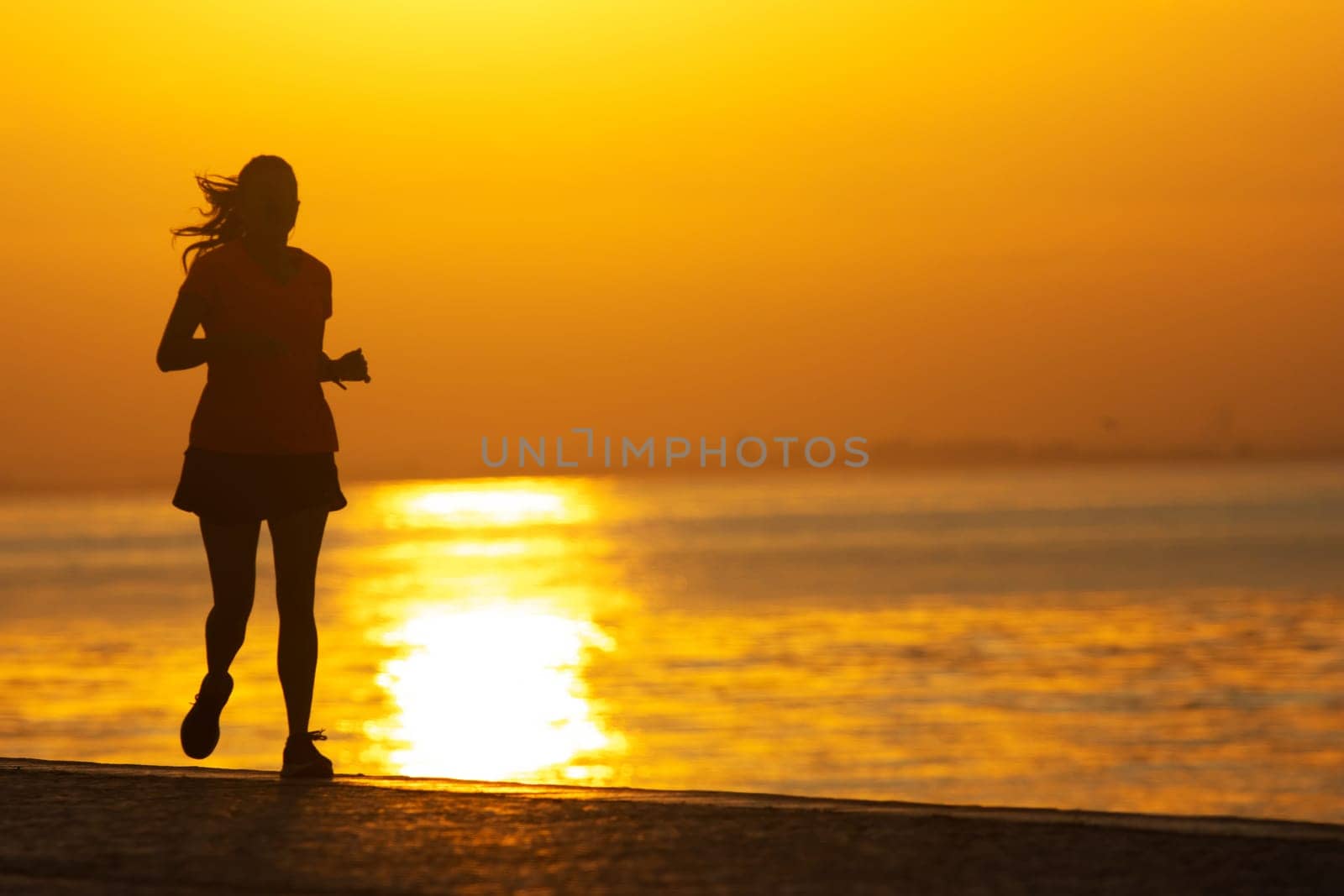 Silhouette of young sportive woman are running on the river. Healthy running and outdoor exercise, morning