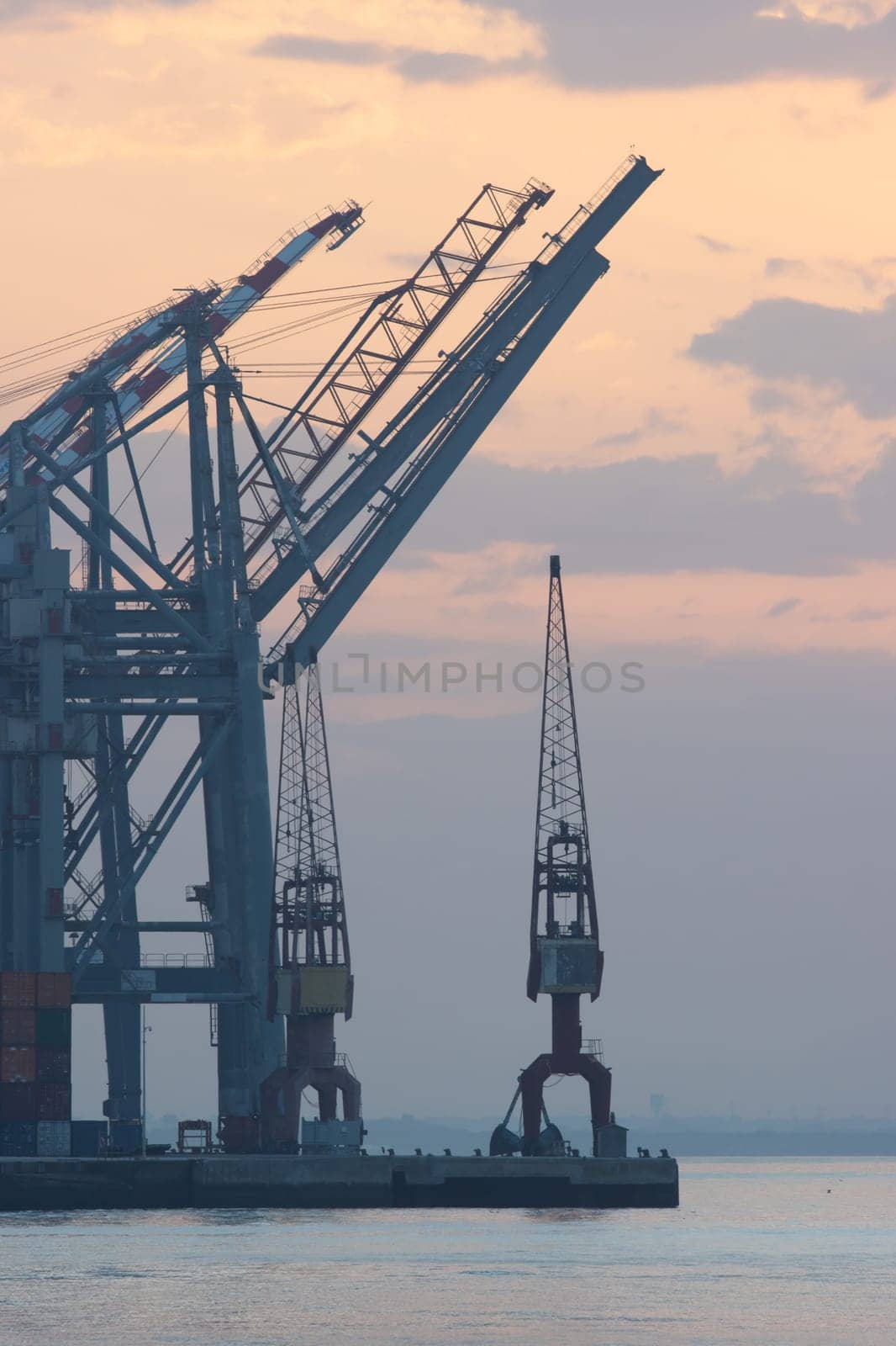 Sea cargo cranes in the port and container terminal of Lisbon, silhouette on sunrise, morning