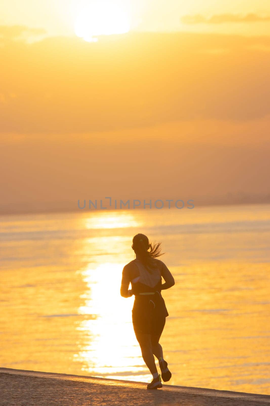 Silhouette of young athletic woman are running on the river, view from the back