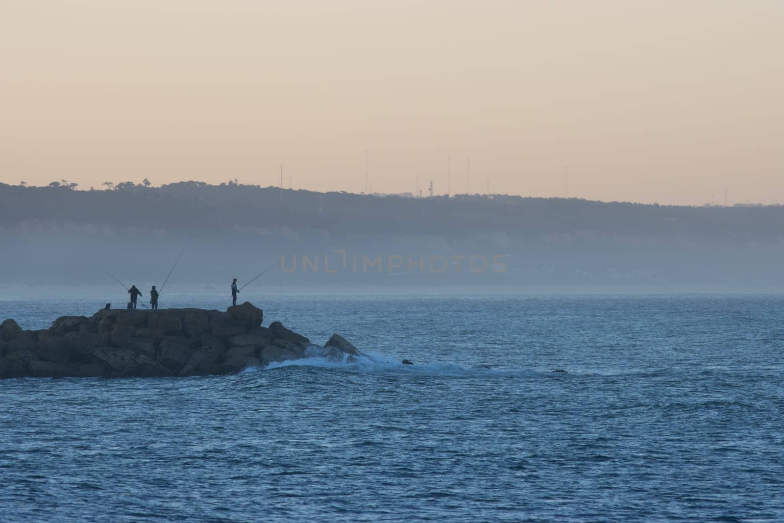 Fishers on the oceans - groupe of men stand on the coast of the sea with fishing rod at sunrise, landscape