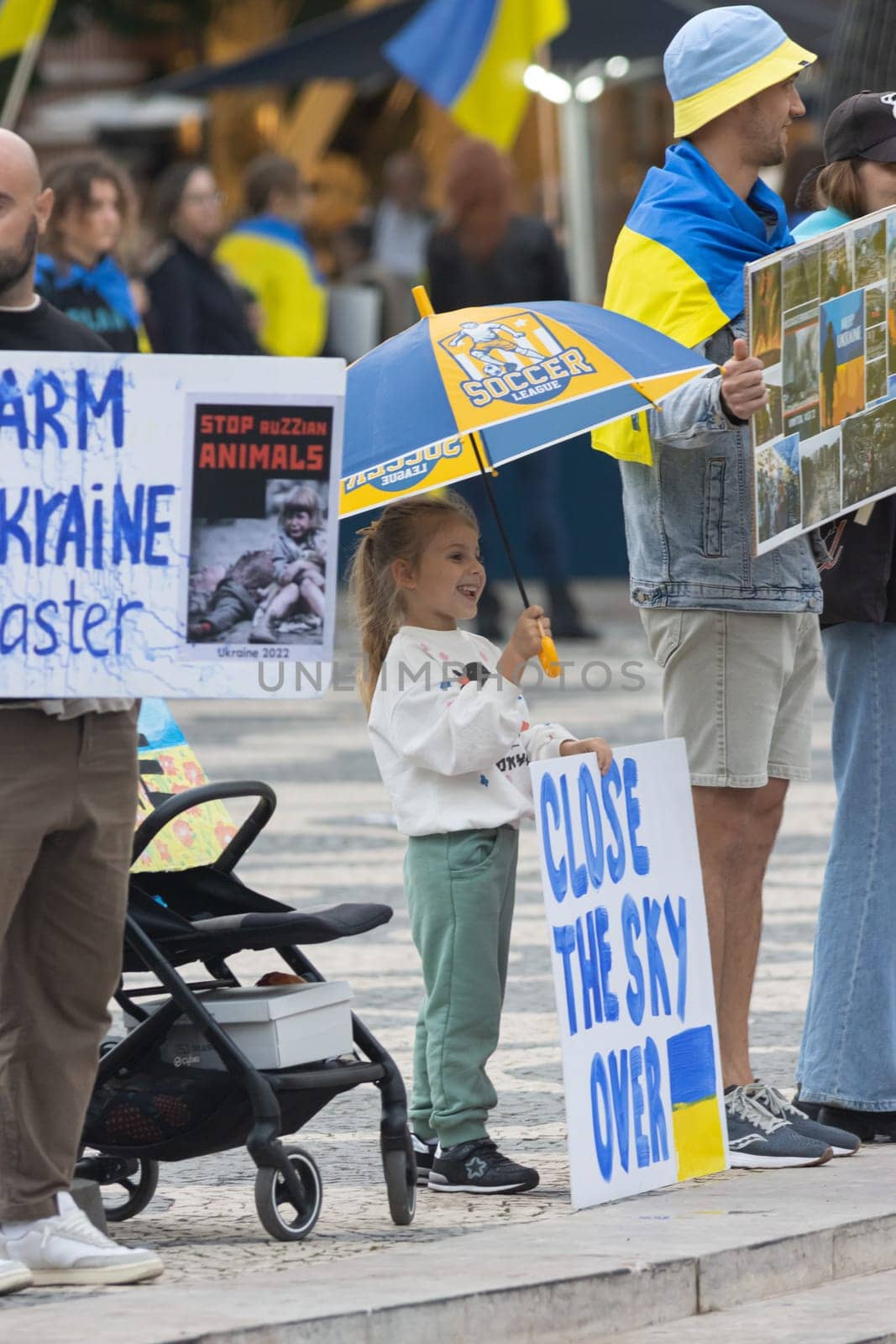 10-29-2022 LISBON, PORTUGAL: Ukrainian protest in Lisbon - little girl under a blue-yellow umbrella holds a poster CLOSE THE SKY OVER UKRAINE. Mid shot