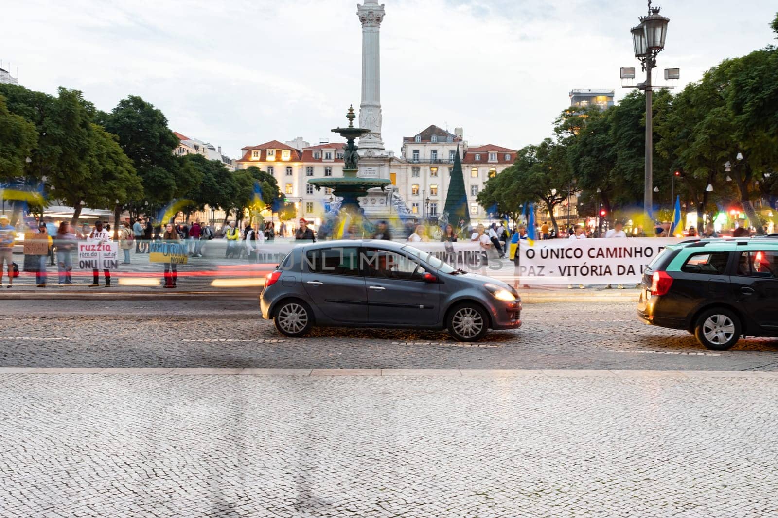 10-29-2022 LISBON, PORTUGAL: Ukrainian protest at Lisbon Square next to the roadway - a car drives past people holding posters. Mid shot