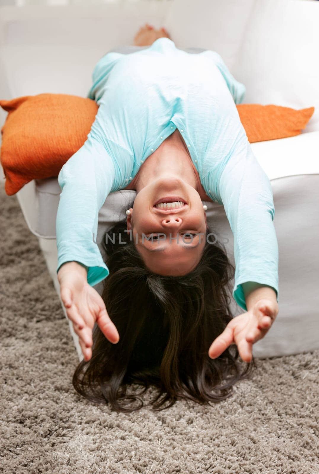 young long haired woman stretching on her sofa relaxing, smiling and rising her hands towards camera