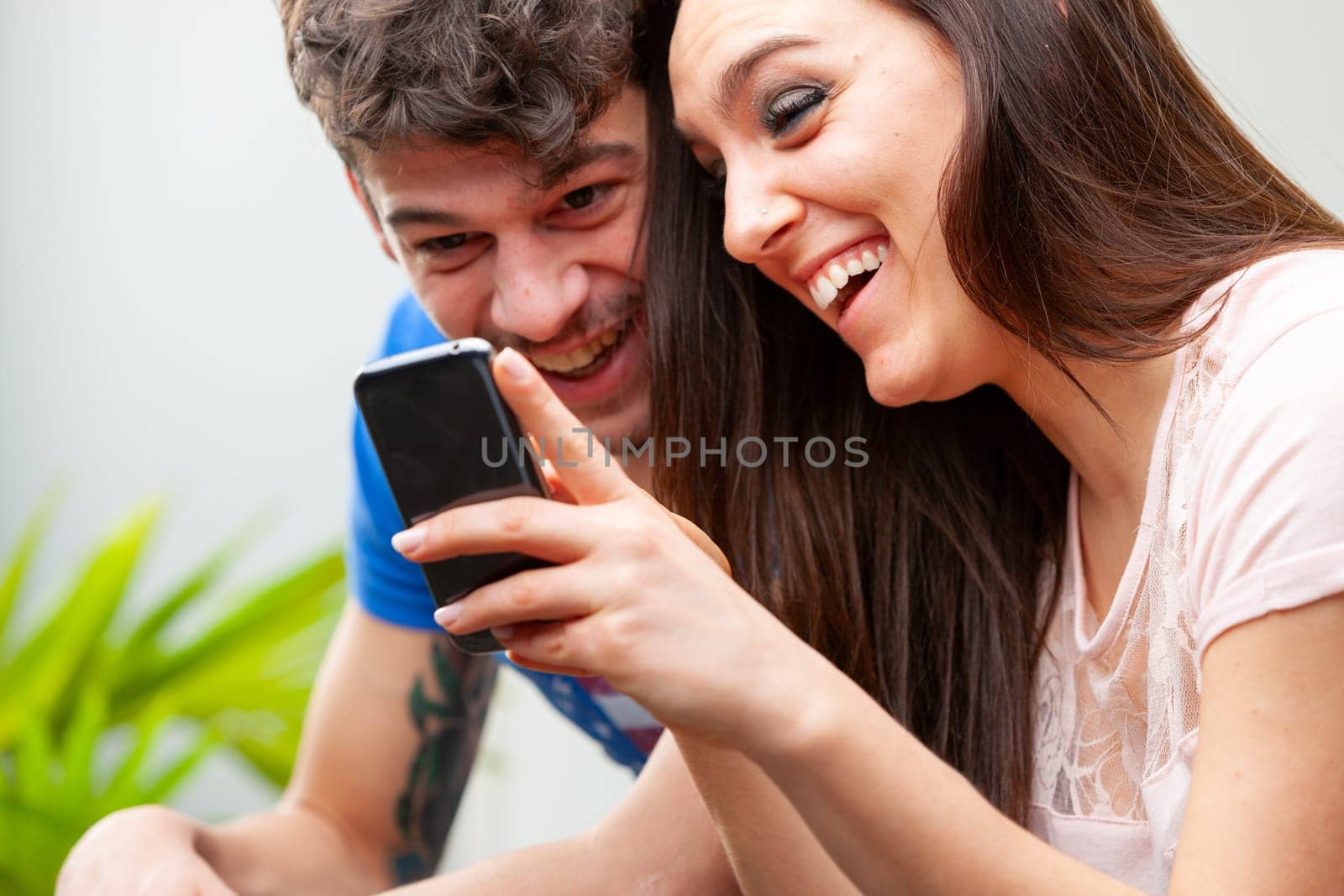 Young couple laughing happily together as they watch media together on her mobile phone in a close up cropped view with focus to their faces