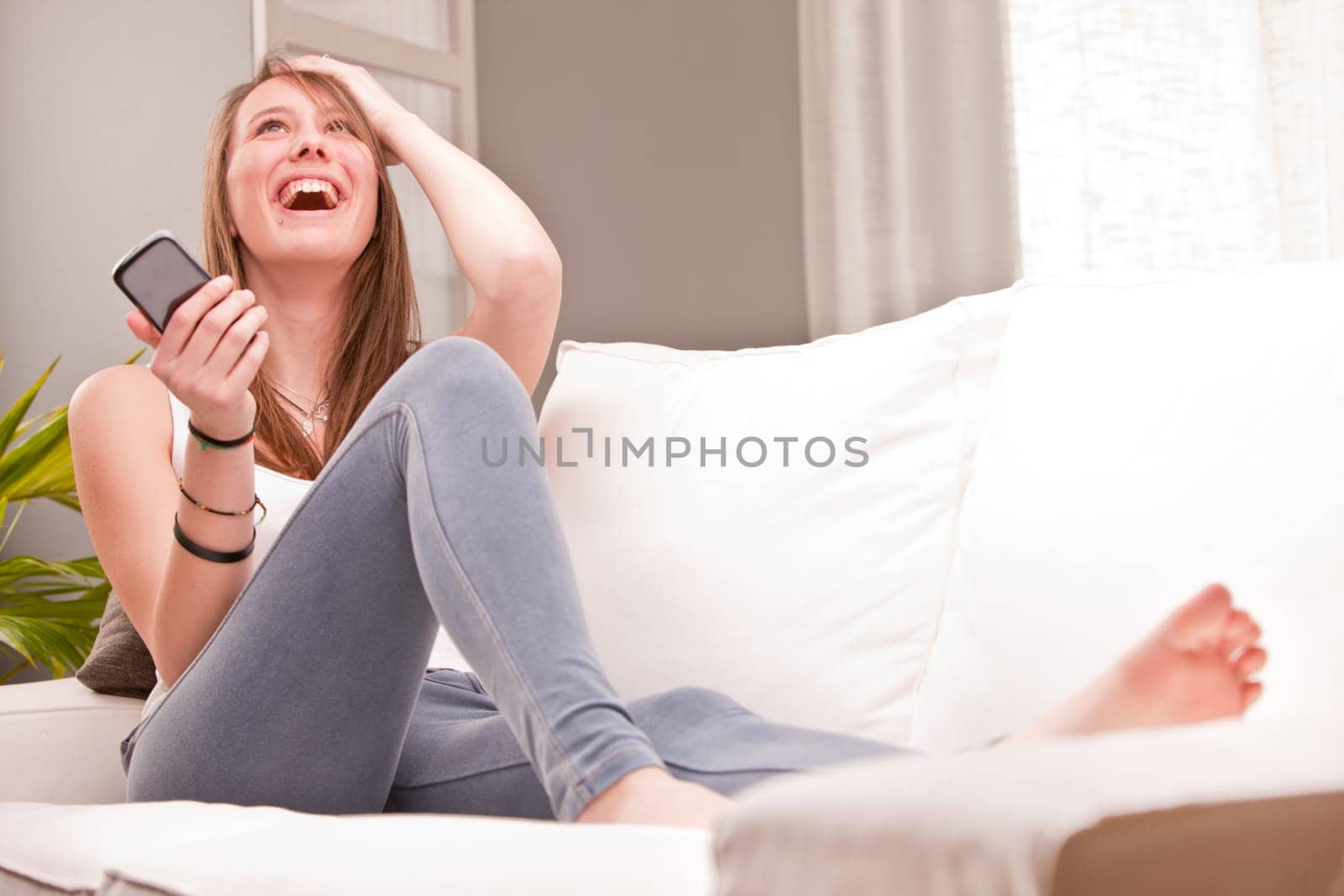 smiling girl using a mobile phone at home in her living room on her sofa
