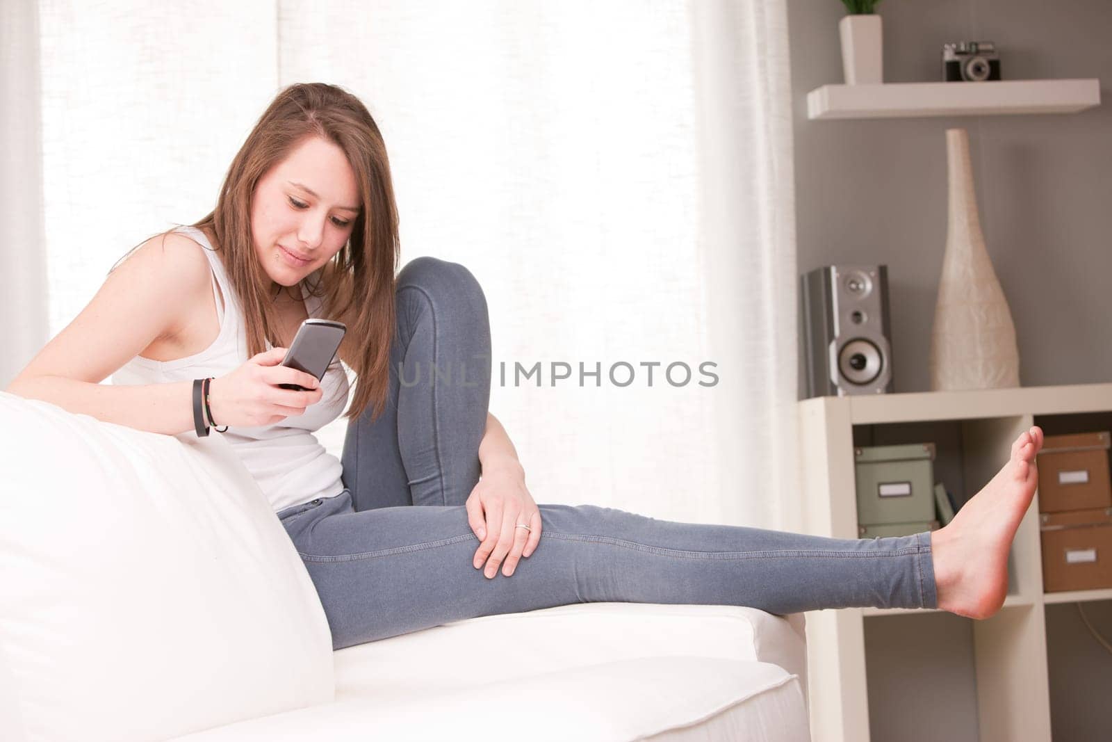 smiling girl using a mobile phone at home in her living room on her sofa