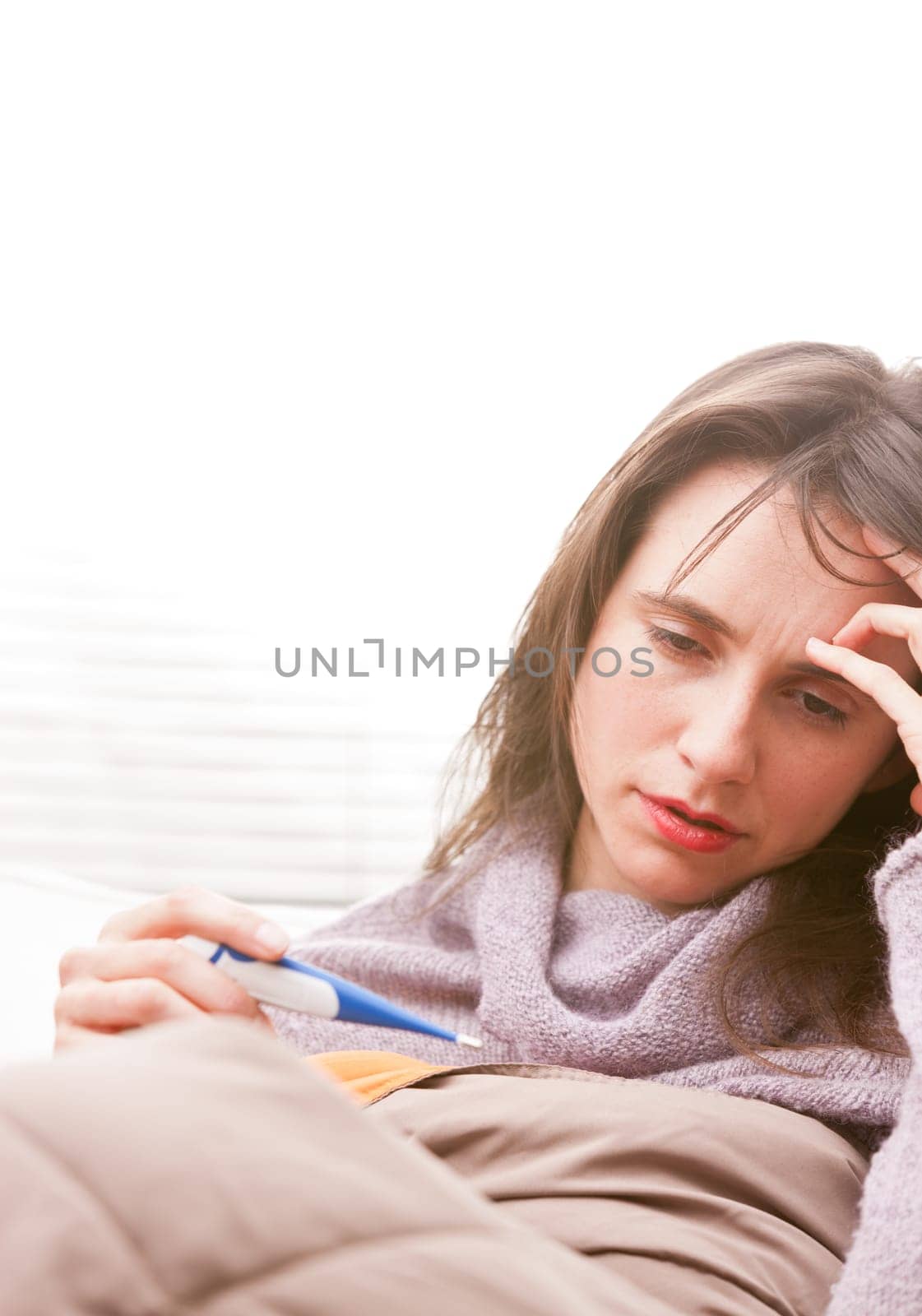 headache and illness of a young woman on a couch in her living room checking a termometer