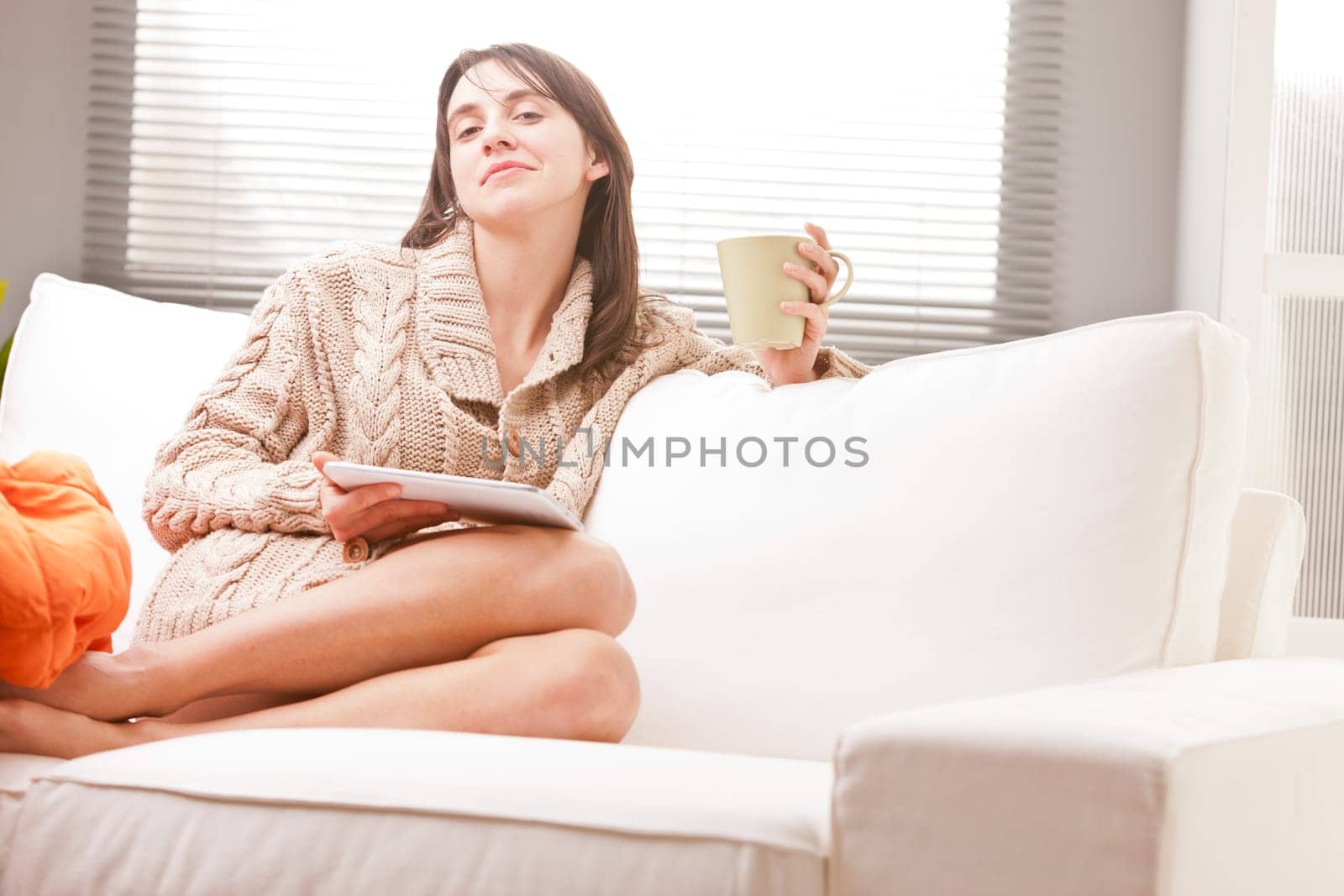 woman using tablet and drinking tea on a sofa in her living room in full relax