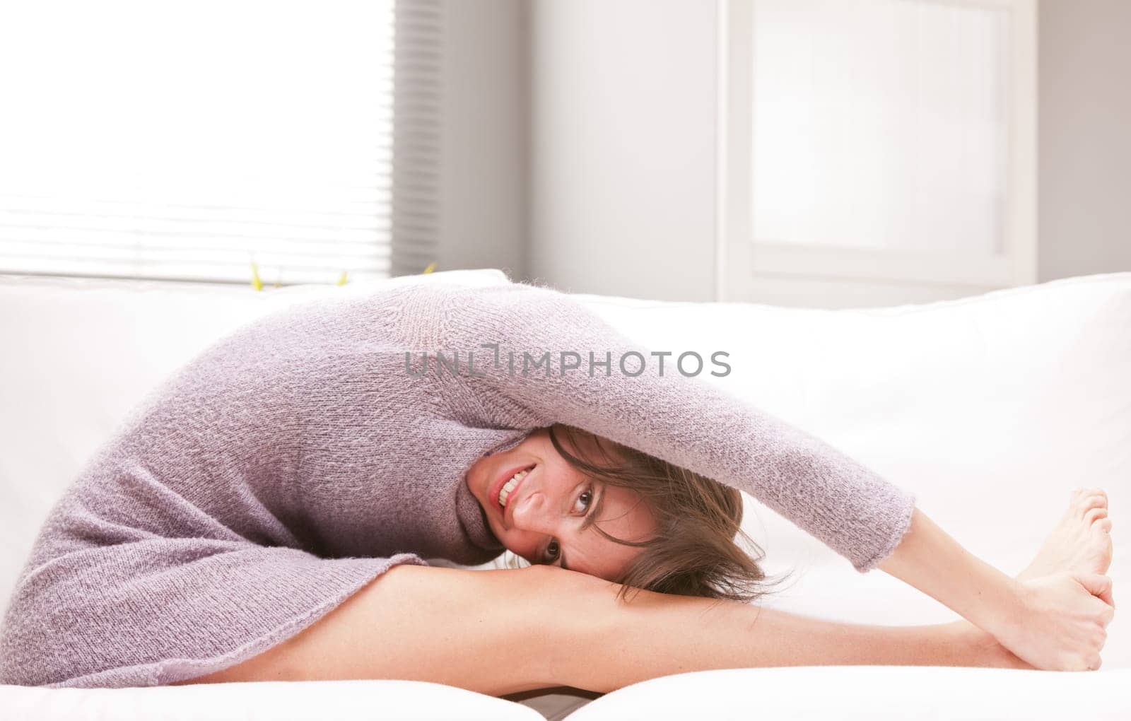 young smiling woman practicing some exercises and stretching on her sofa in her living room