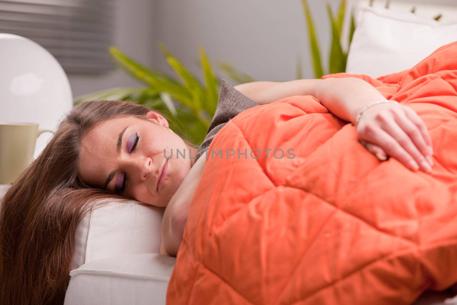 young beautiful sexy woman softly sleeping on her sofa under her warm orange quilt