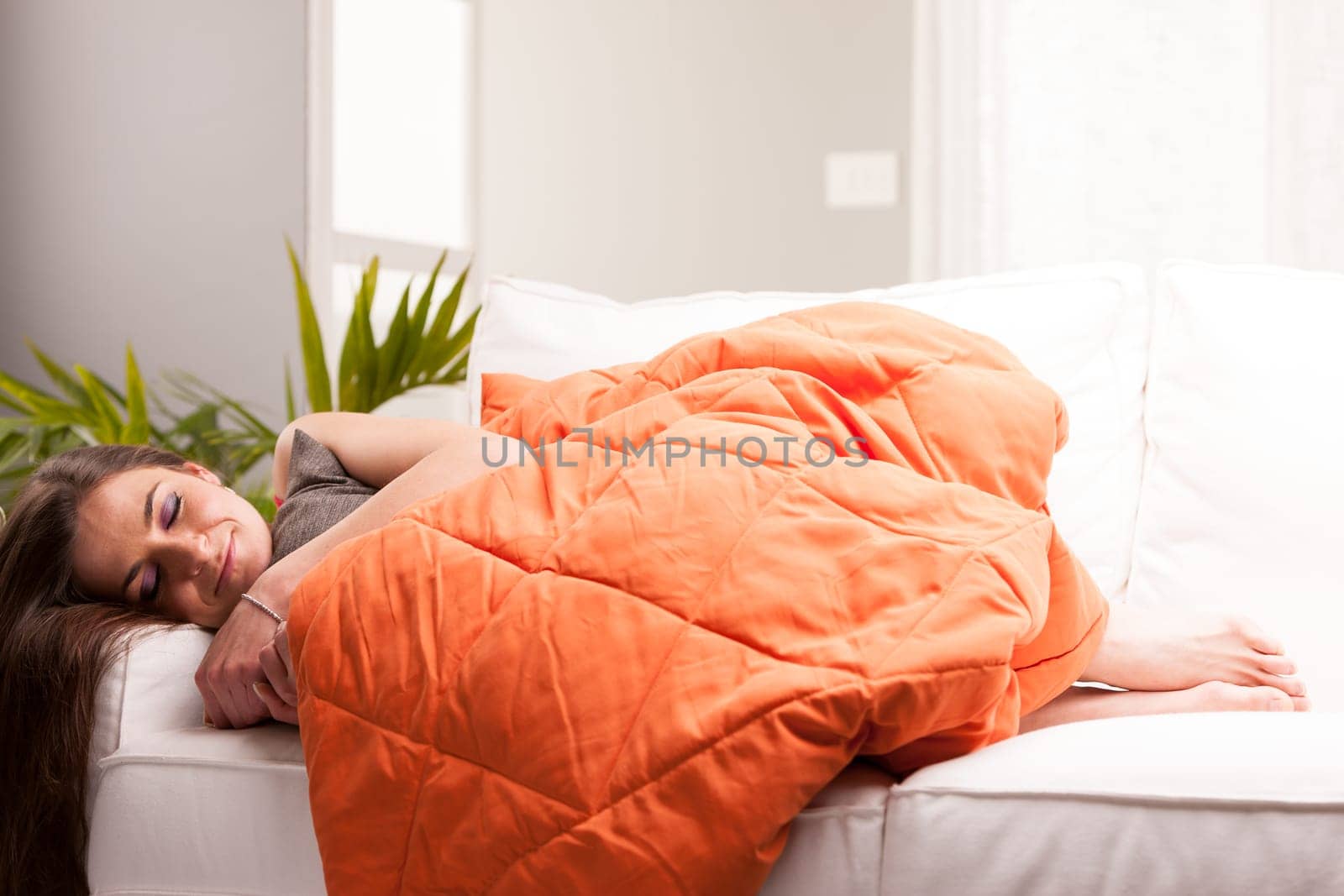 woman sleeping like a baby in her very comfortable living room on her white sofa under an orange quilt