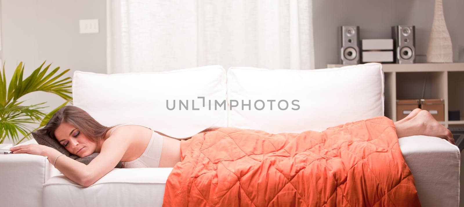 young woman sleeping under an orange quilt softly lying on a sofa in her living room