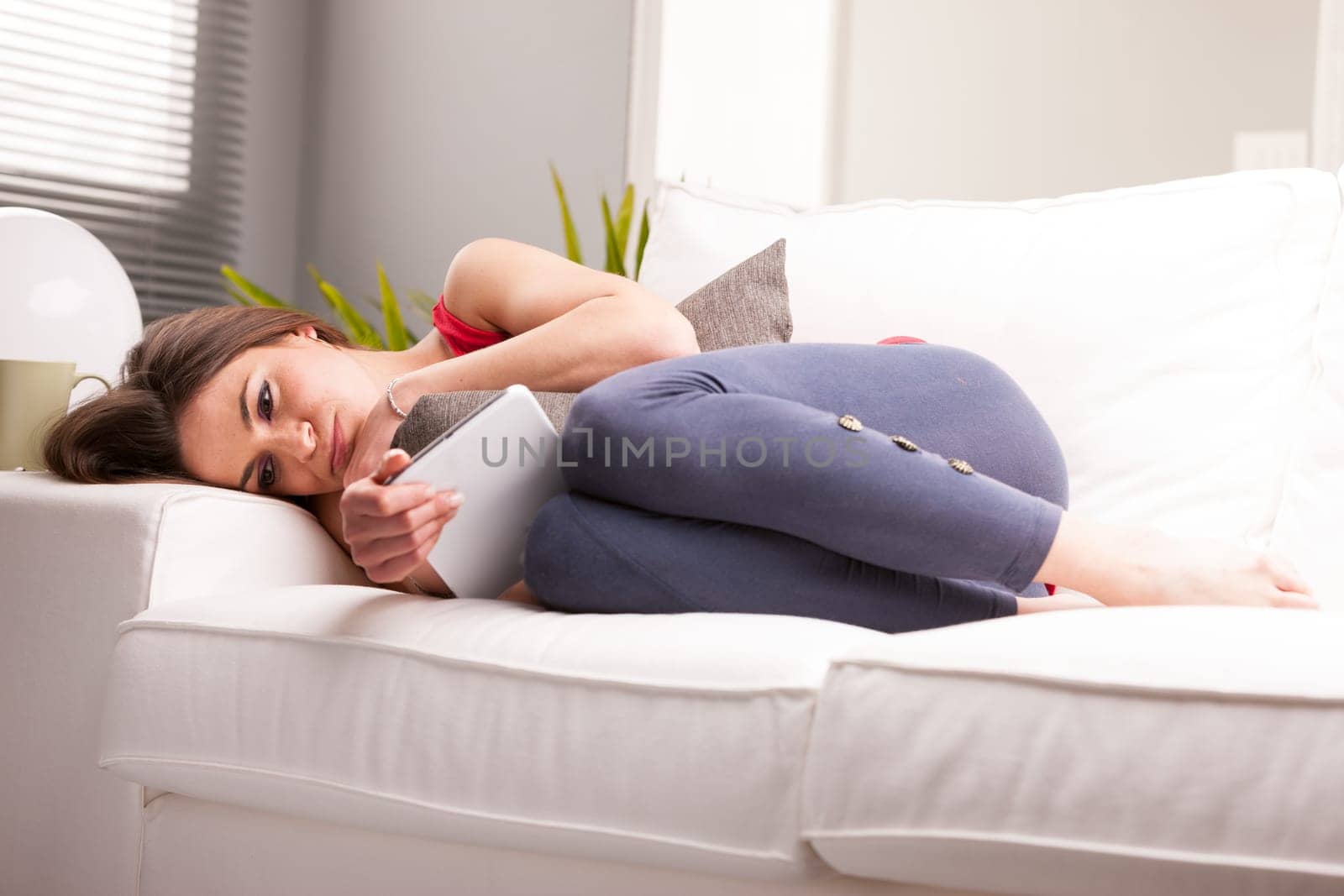woman on a sofa looking worried about something she could have just read on her white digital tablet