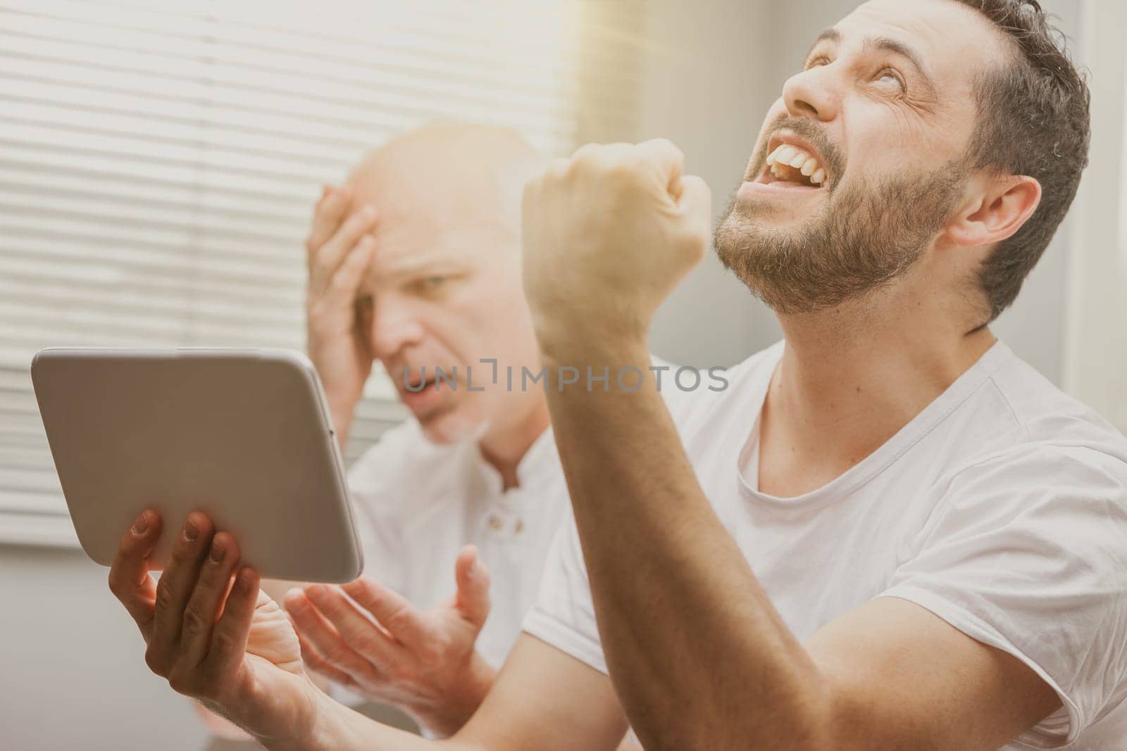 One man looking at his handheld tablet showing dismay as another laughs and cheers in a conceptual image