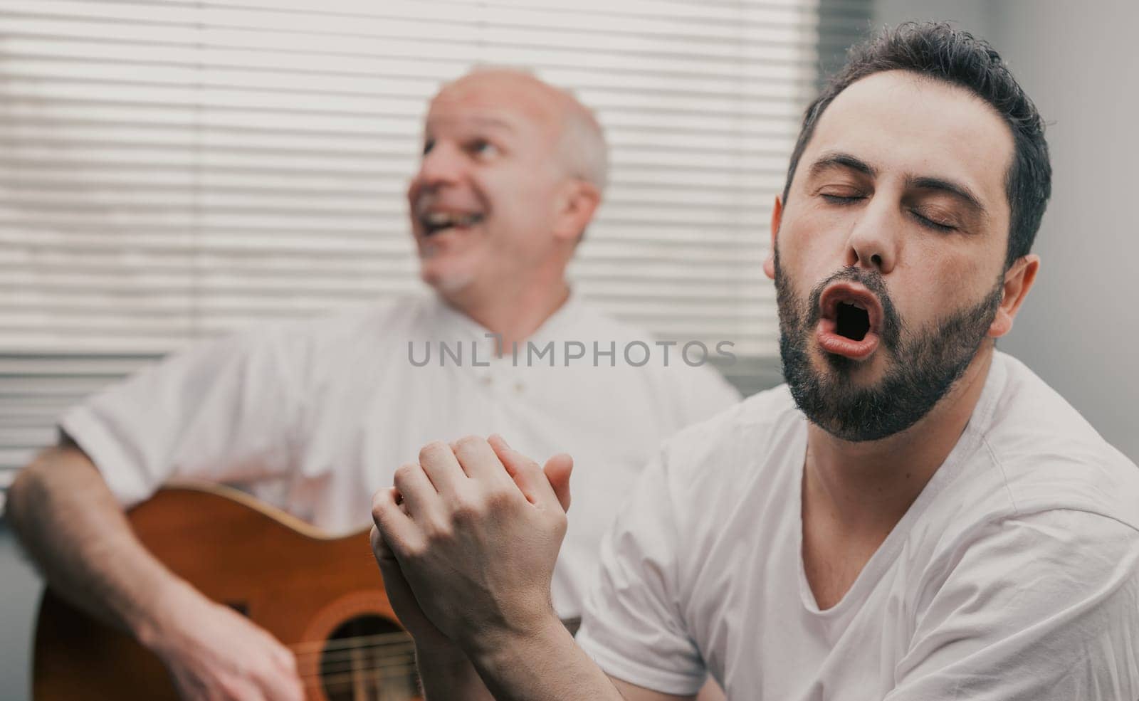 Man singing while his senior father or friend is playing the guitar as a hobby or a funny relaxing activity at home