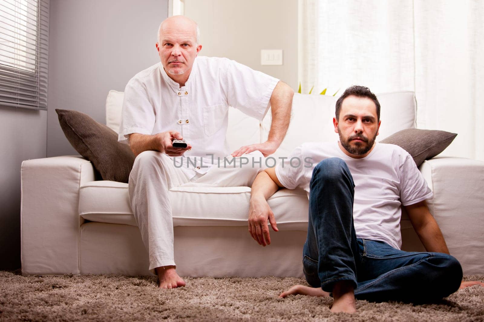 a couple of friends watching sports on tv in a white living room on the sofa