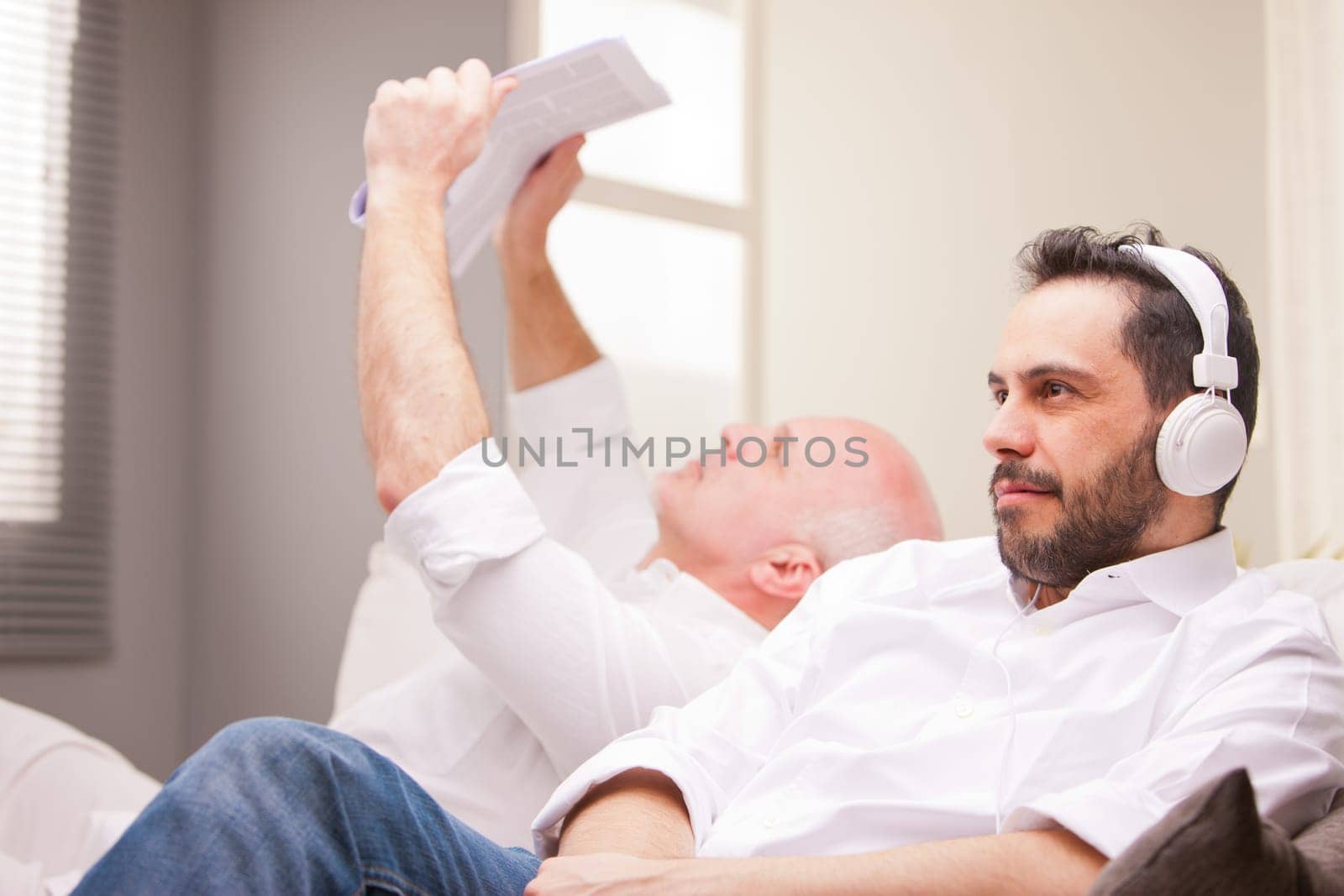 one man reads a newspaper and the other one relaxes listening to music