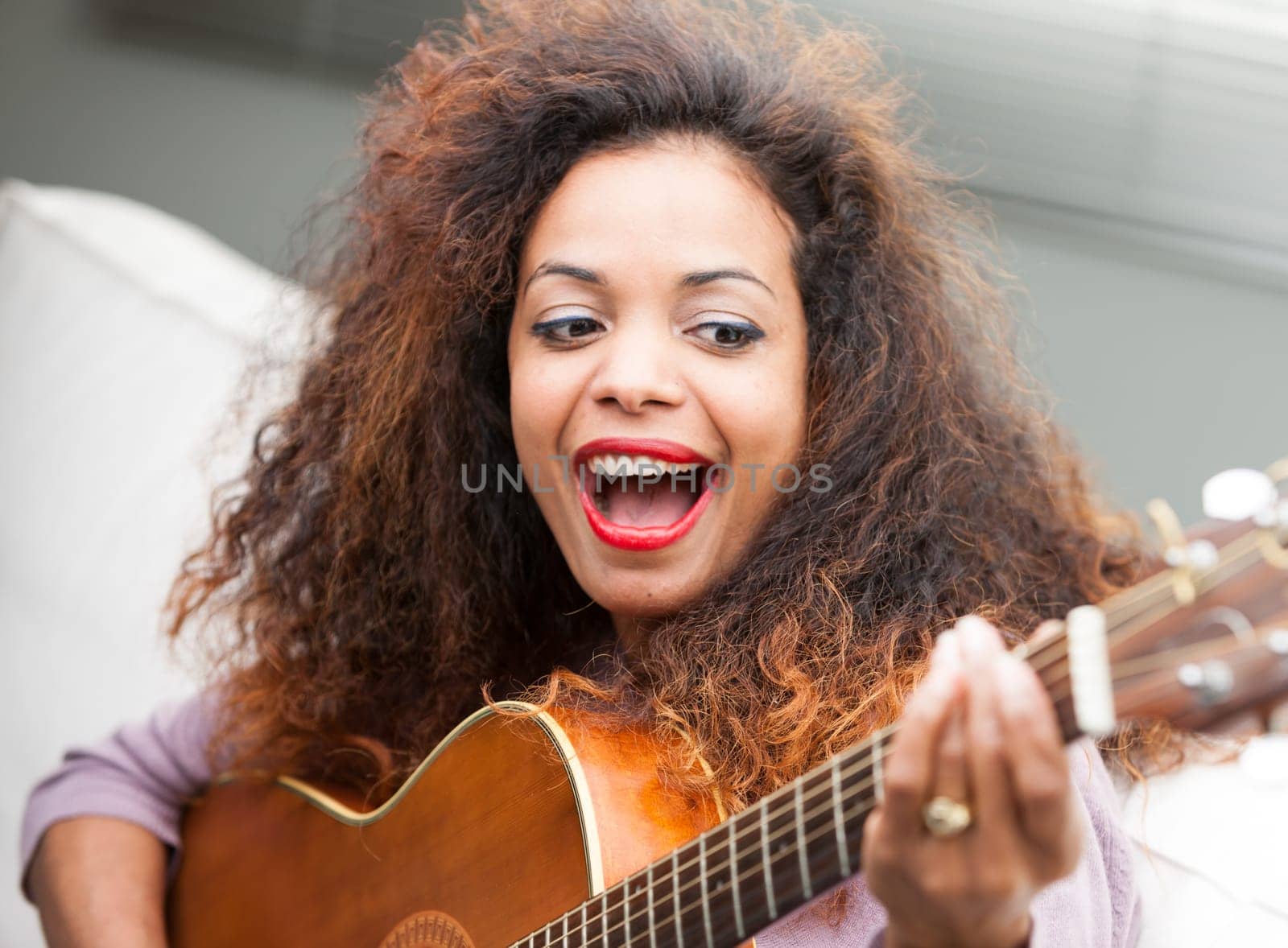 young beautiful afroemerican woman having fun with her guitar on her sofa in her living room