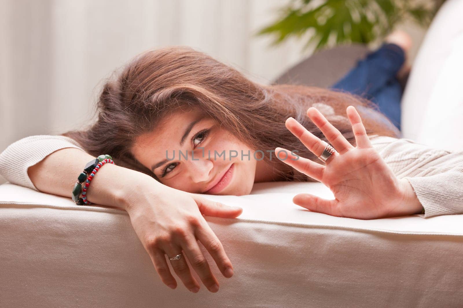 girl waving at you and smiling while standing on a couch in a light coloured living room
