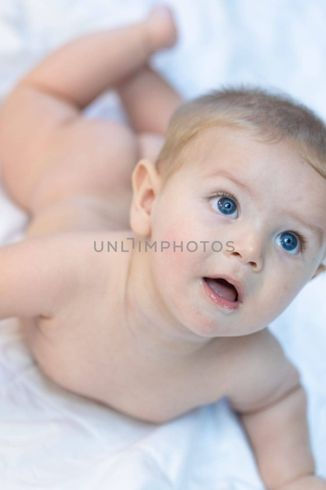 Innocent little baby staring up watching something off to the side with large trusting blue eyes as it lies naked on a bed
